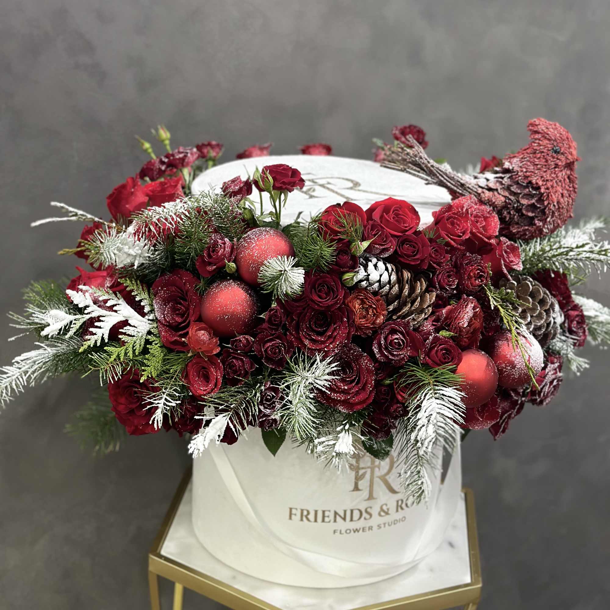 Red roses and pinecones in a white hatbox with a bird ornament