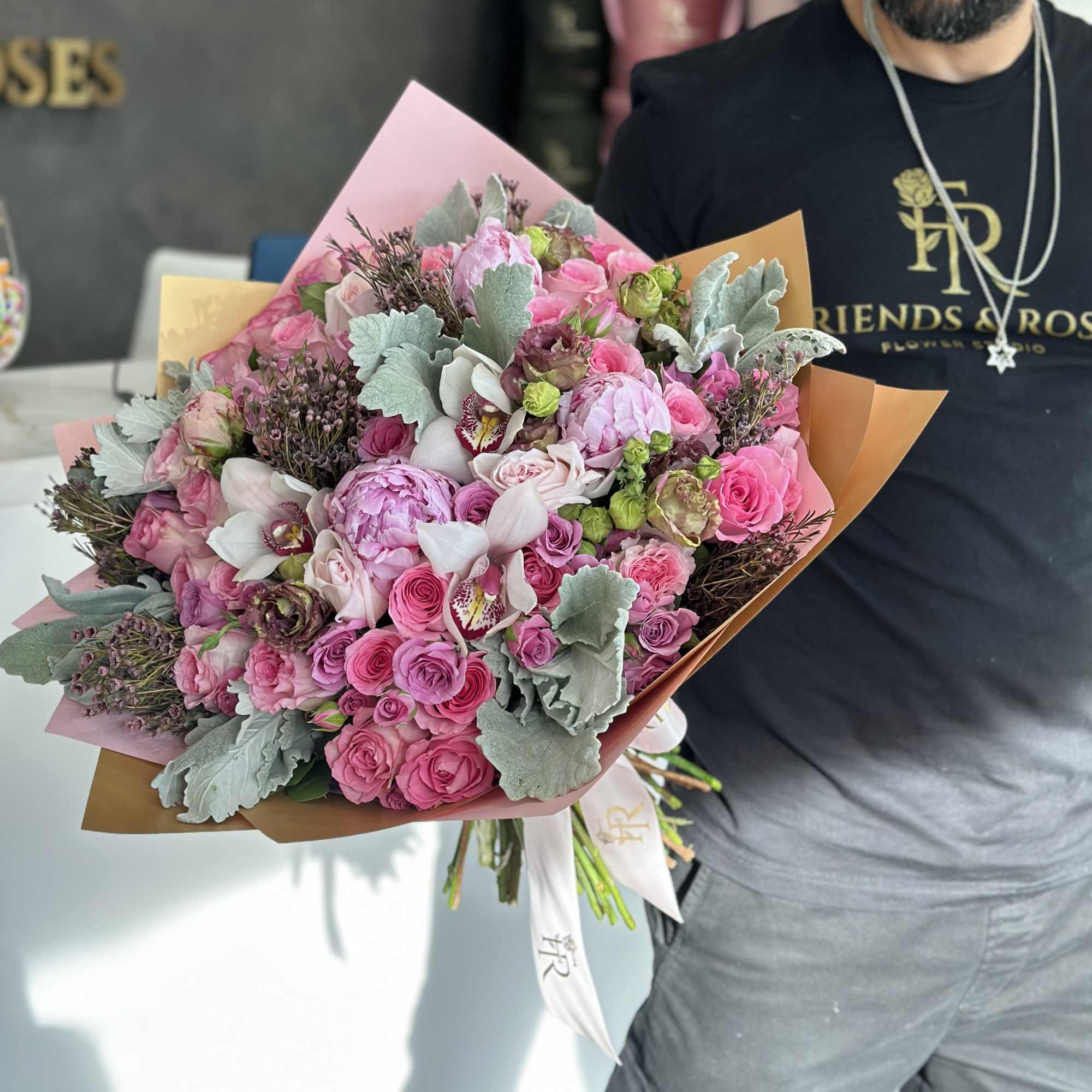 Large pink bouquet with roses, orchids, and pale foliage wrapped in paper