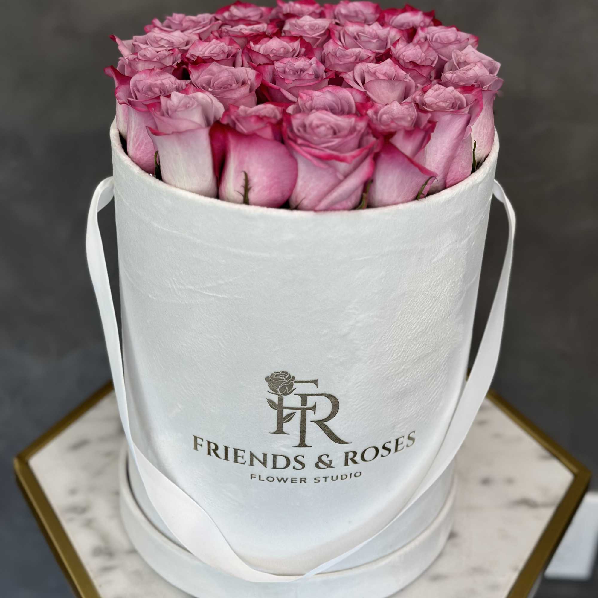 Pink roses arranged in a white round hat box with ribbon handles