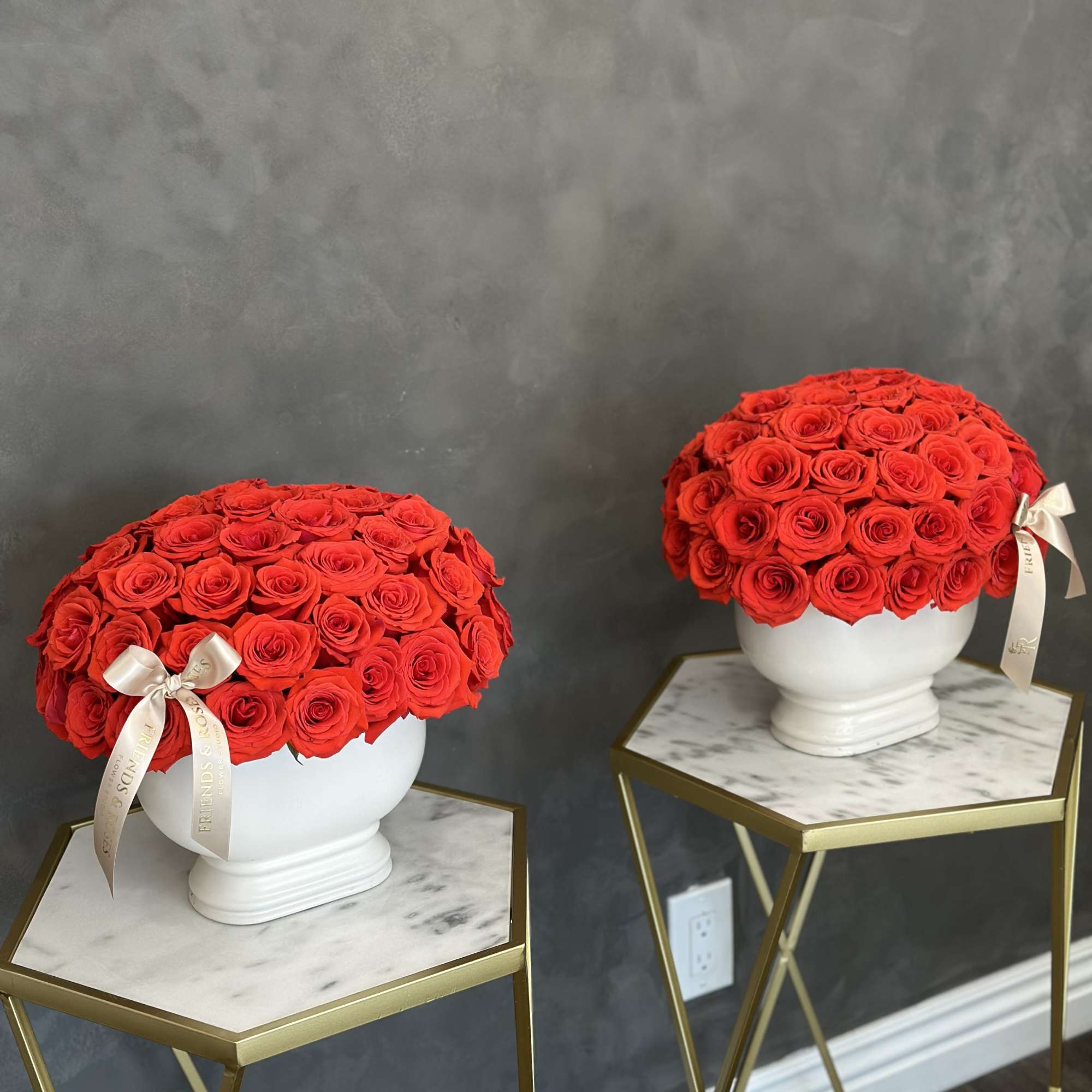 Two red rose arrangements in white urns on marble-top stands