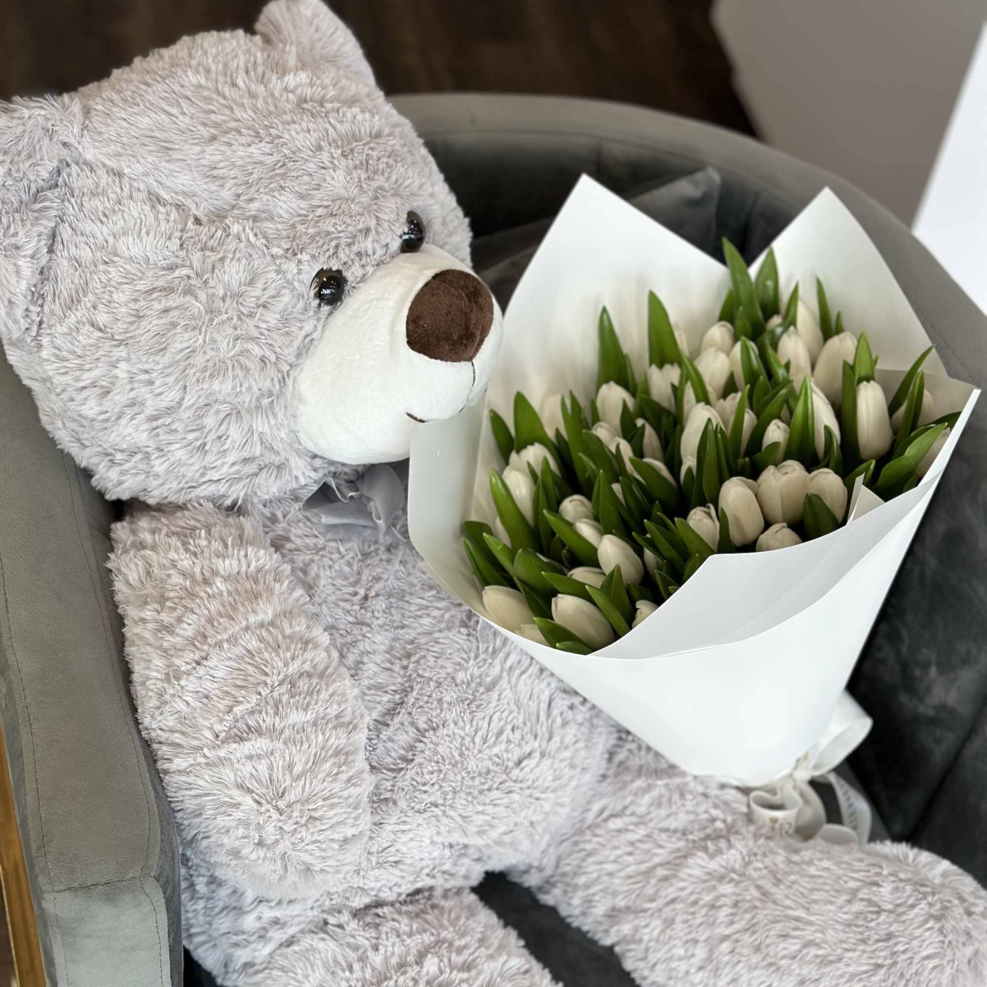 A plush teddy bear holds a bouquet of white tulips.