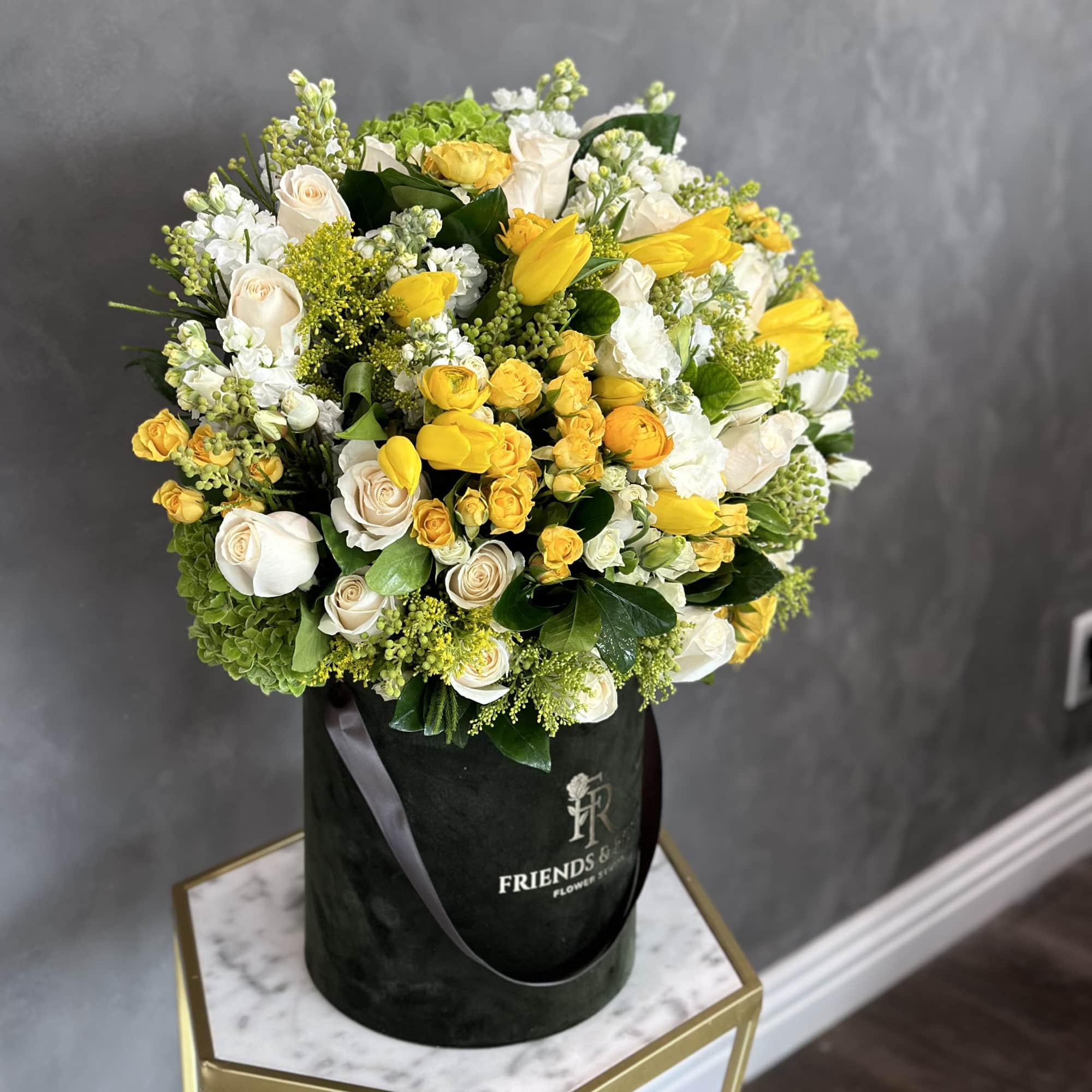 Yellow and white roses arranged in a black hatbox.