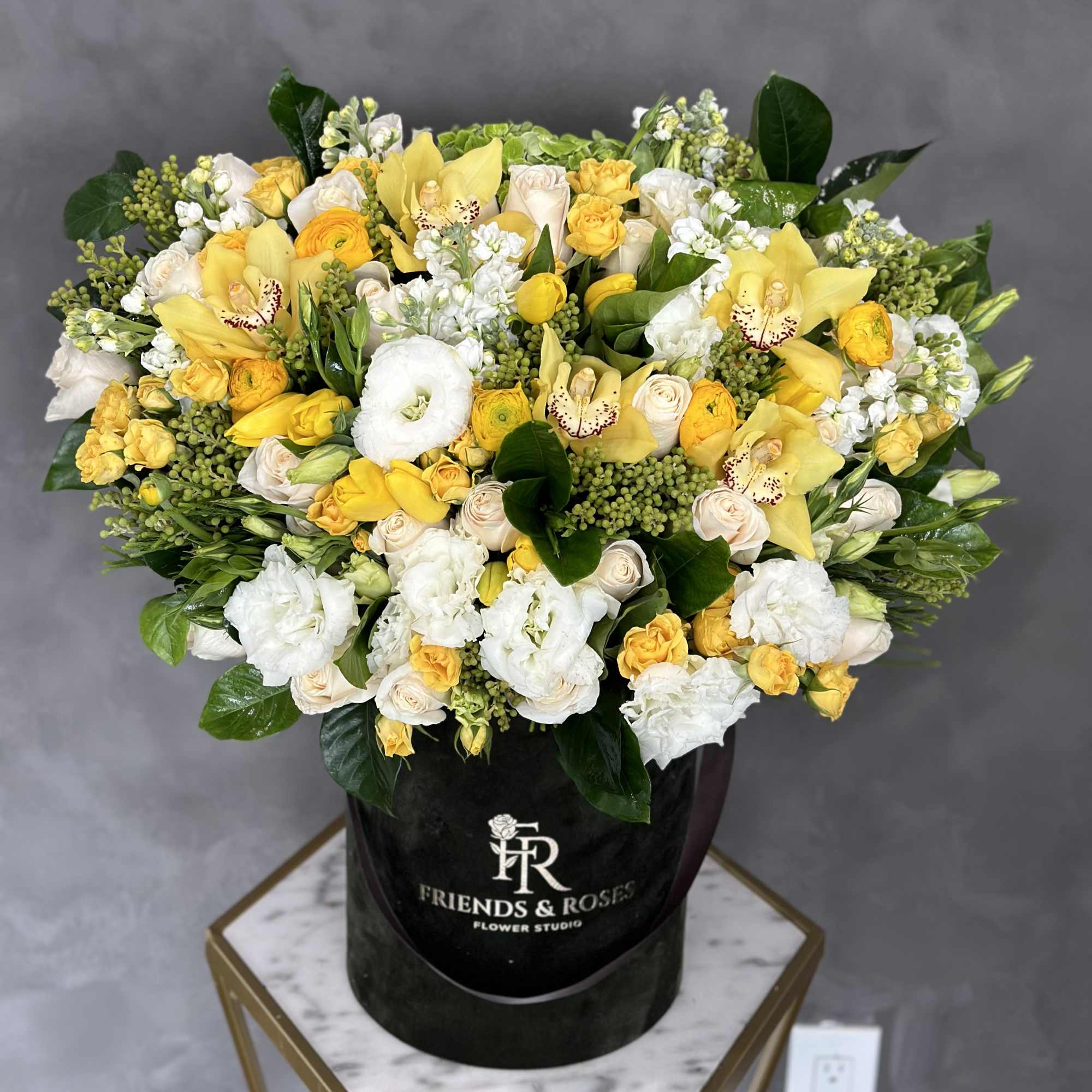 Yellow and white floral arrangement in a black hat box