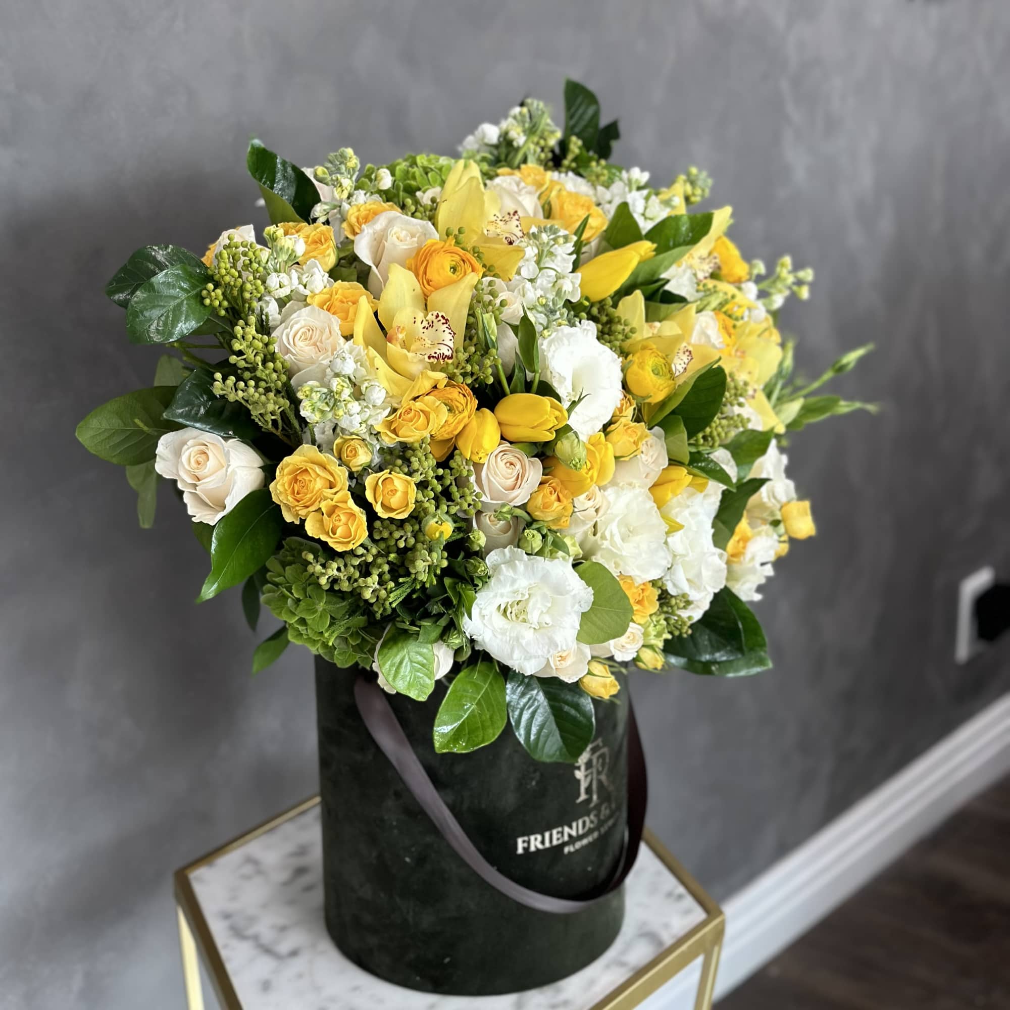 Yellow and white bouquet in a dark round box