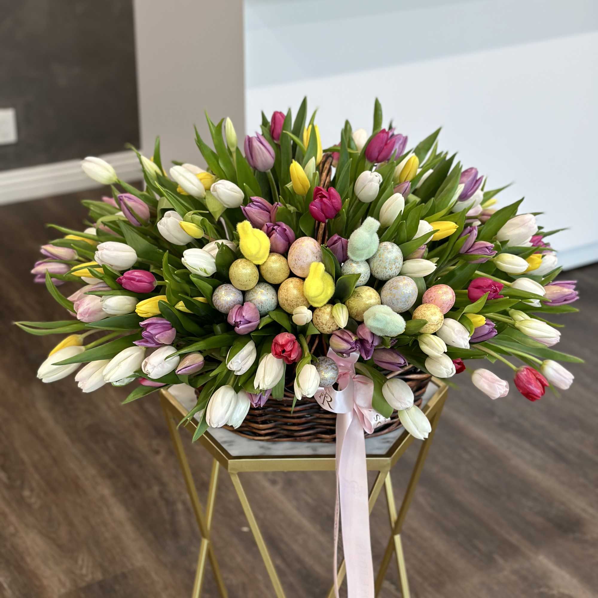 Basket of multicolored tulips with pastel Easter eggs and a pink ribbon