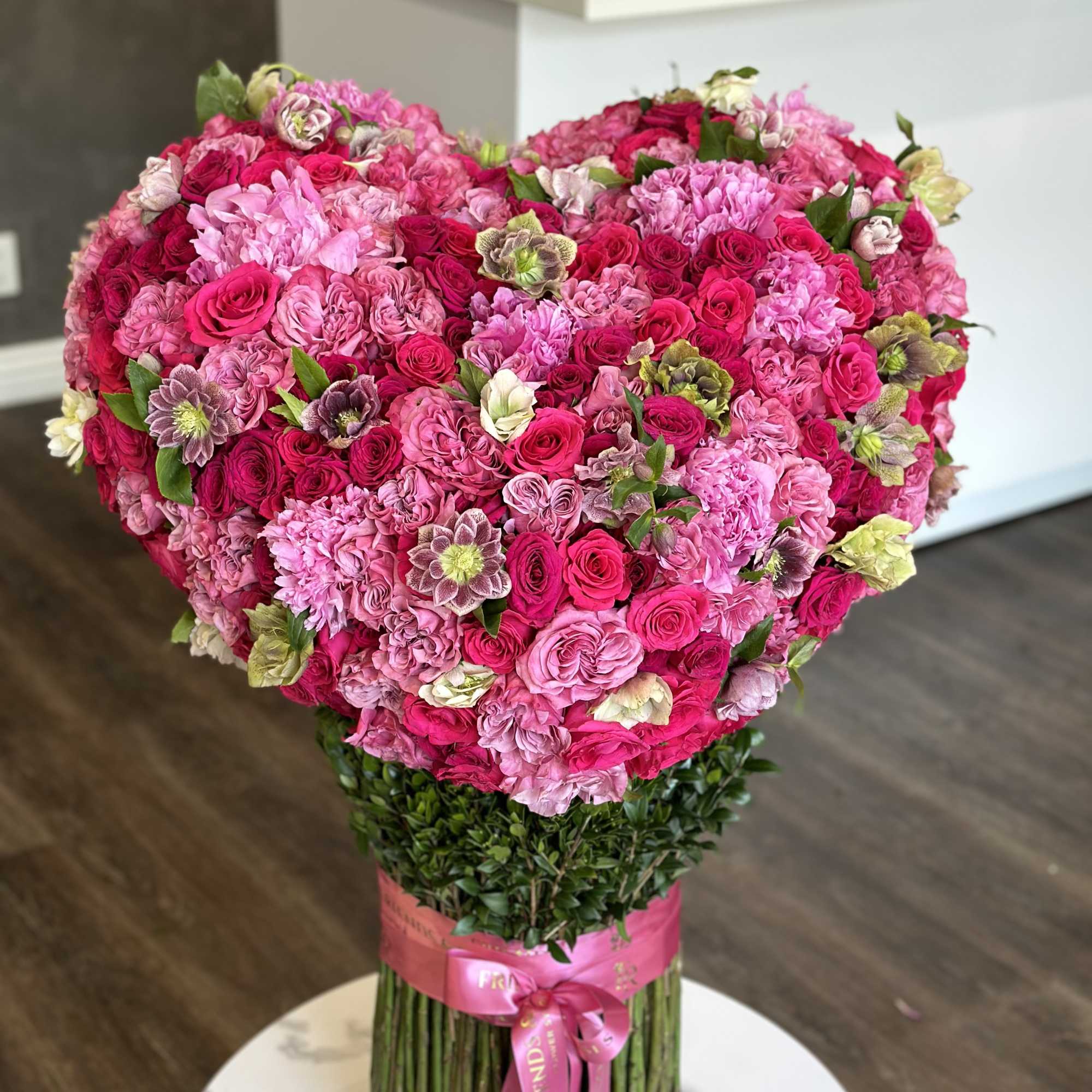 Large heart-shaped bouquet of pink and magenta roses with a ribbon-wrapped stem bundle