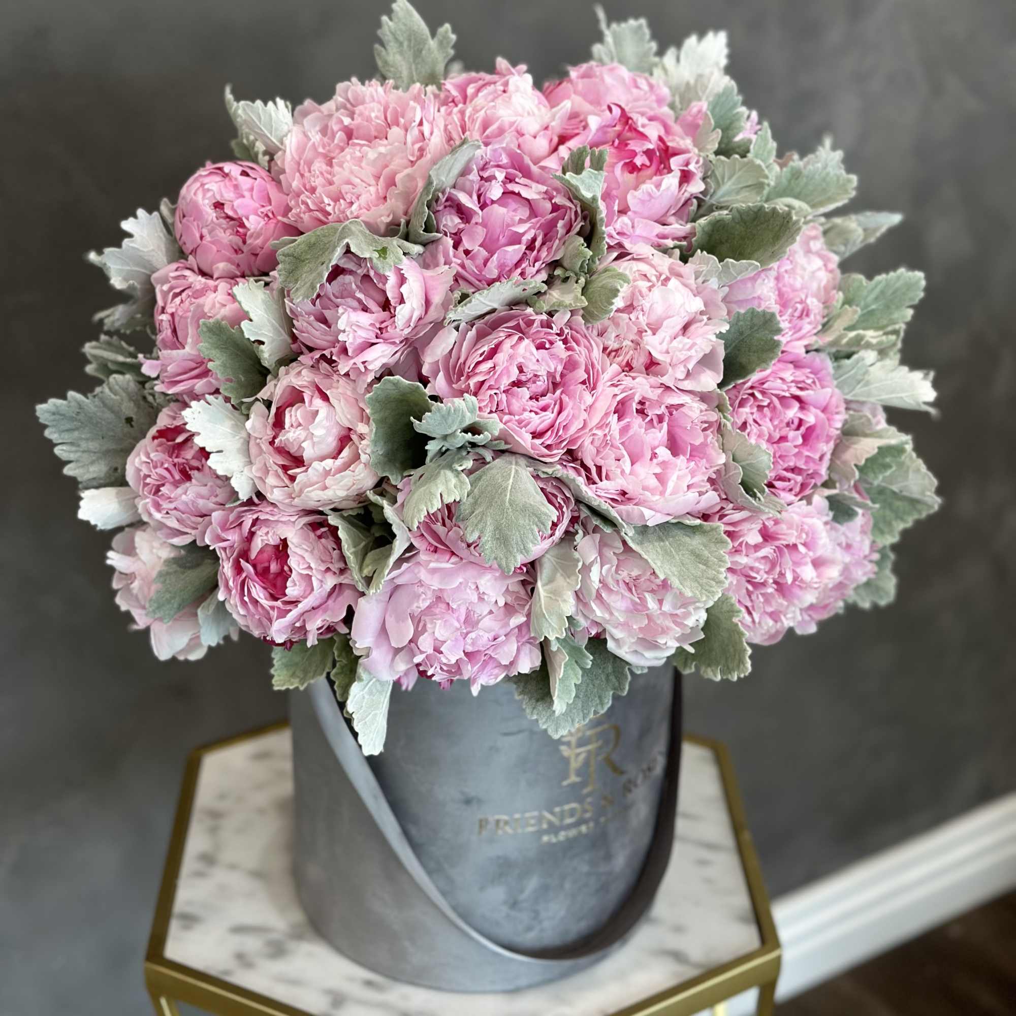 Pink peony bouquet in a gray hatbox with silvery foliage