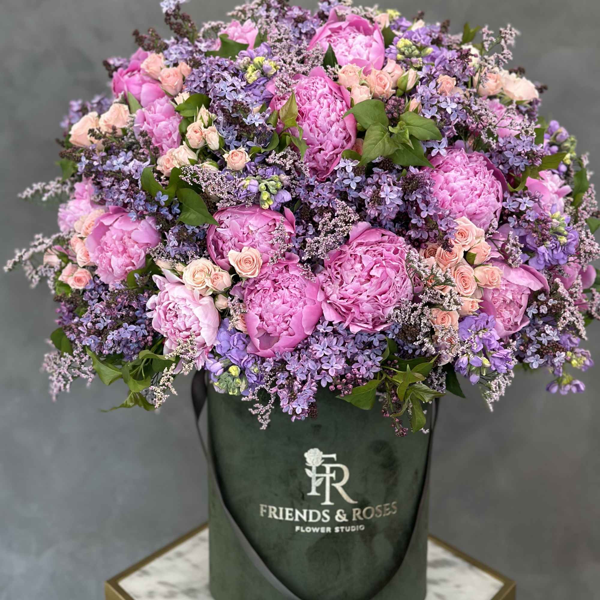 Large pink and lavender flower arrangement in a dark green hatbox
