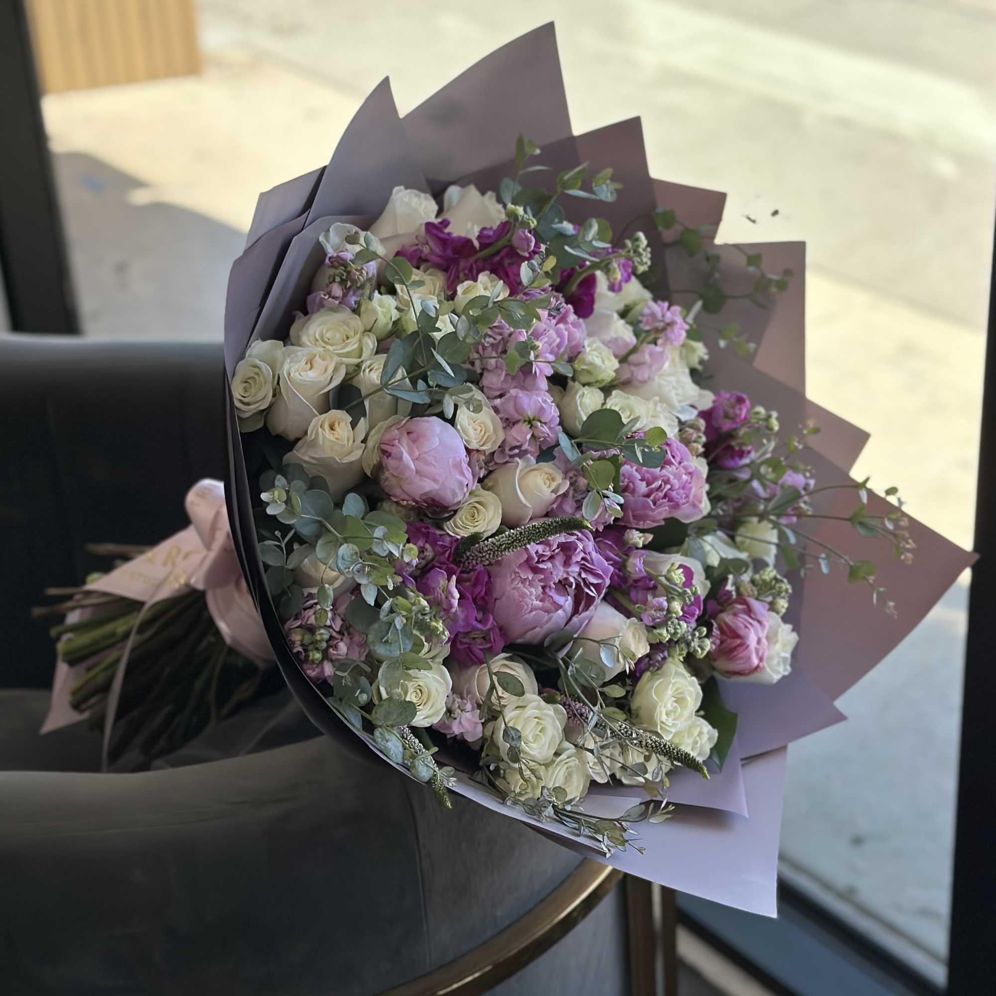 Bouquet of pink and white roses with purple blooms wrapped in mauve paper