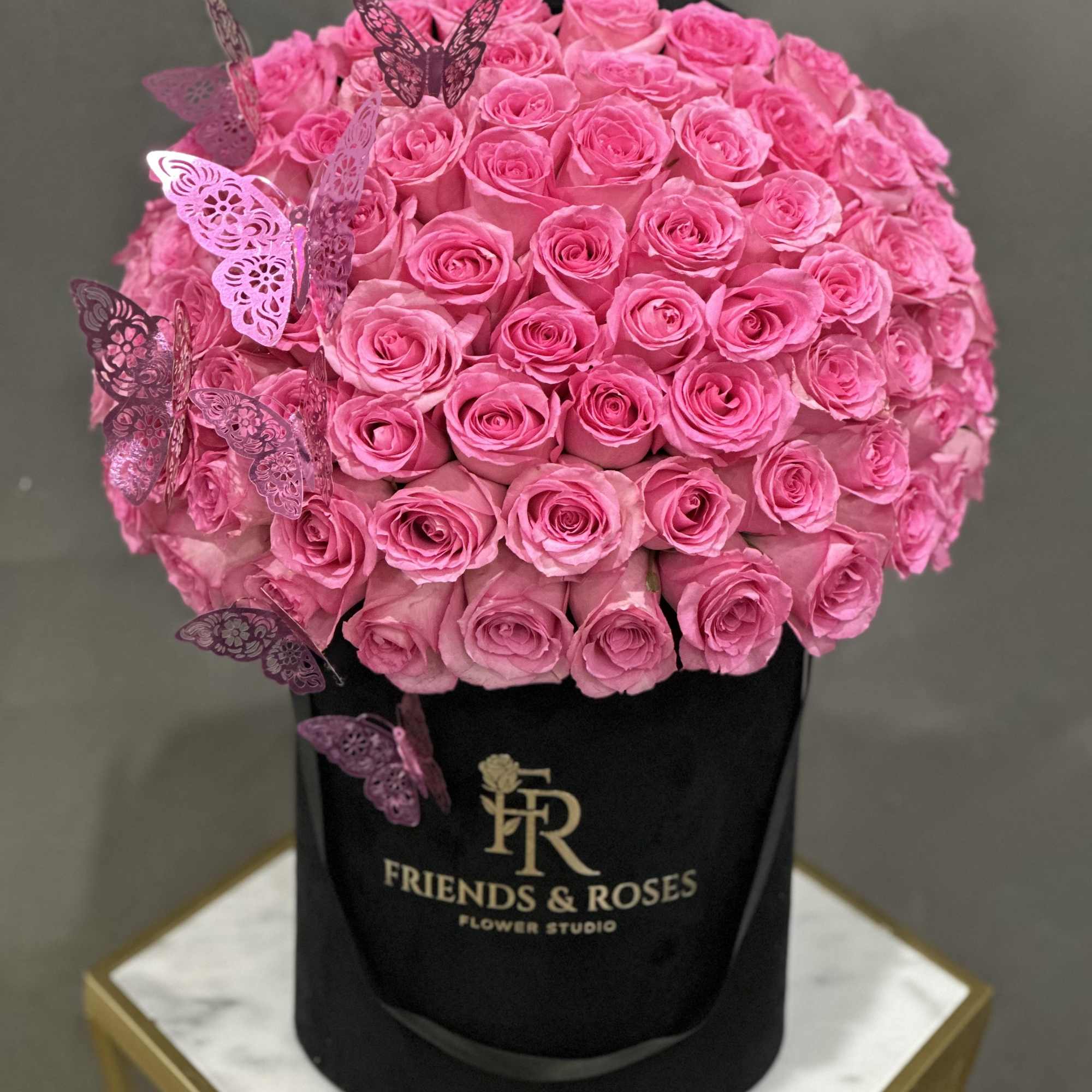Pink roses arranged in a black hatbox with decorative butterfly picks