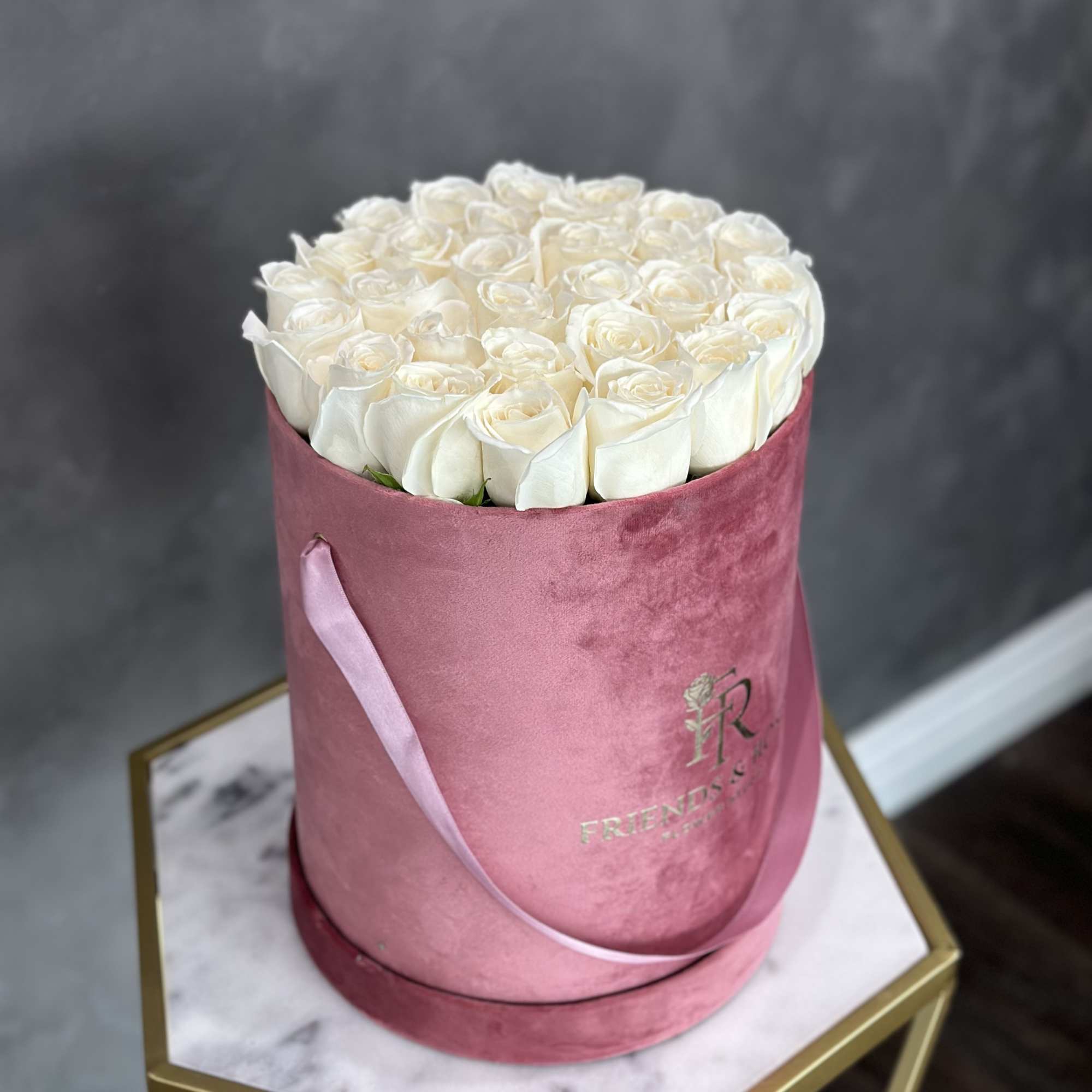 White roses arranged in a pink round box with a ribbon.