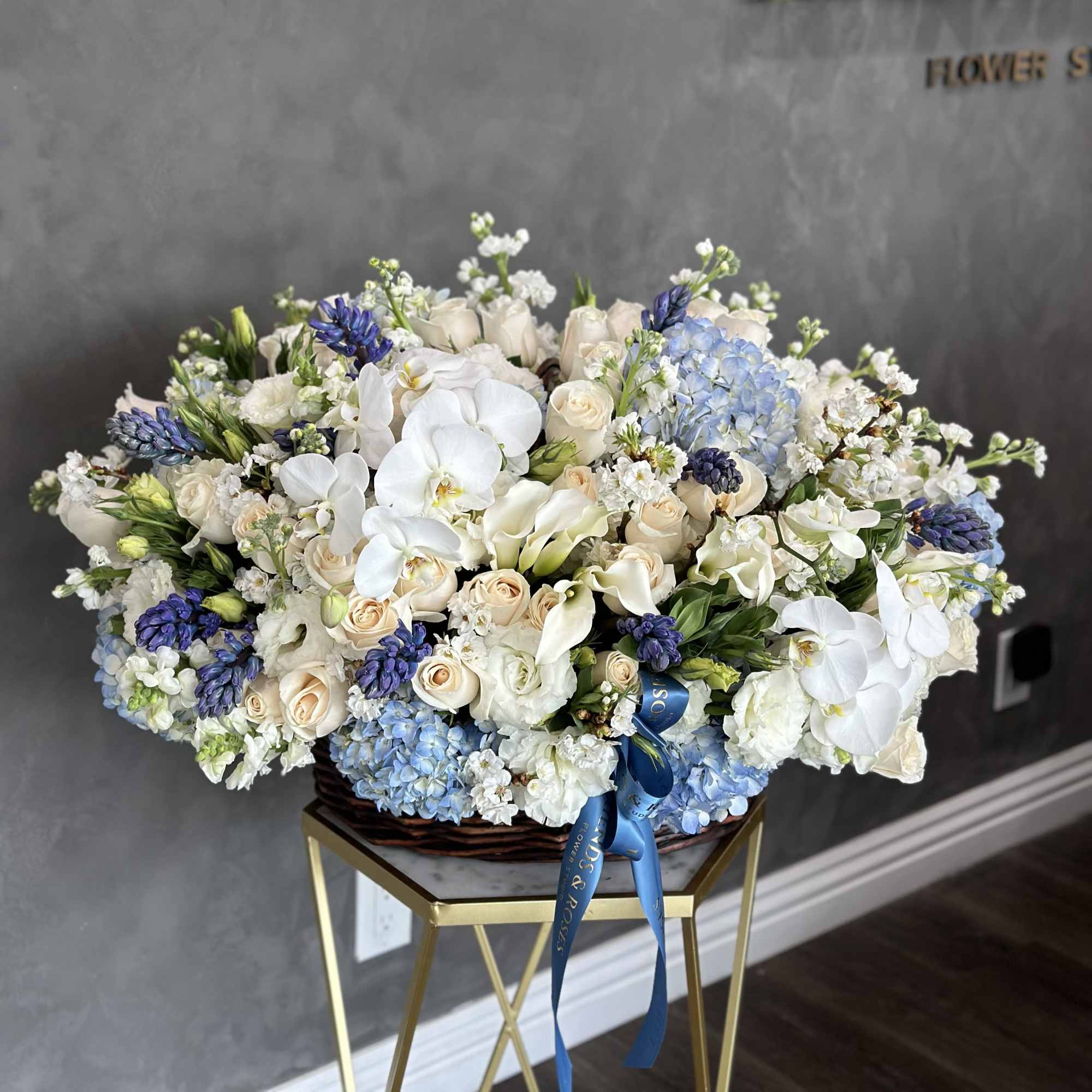 Large basket arrangement of white orchids, cream roses, and blue hydrangeas