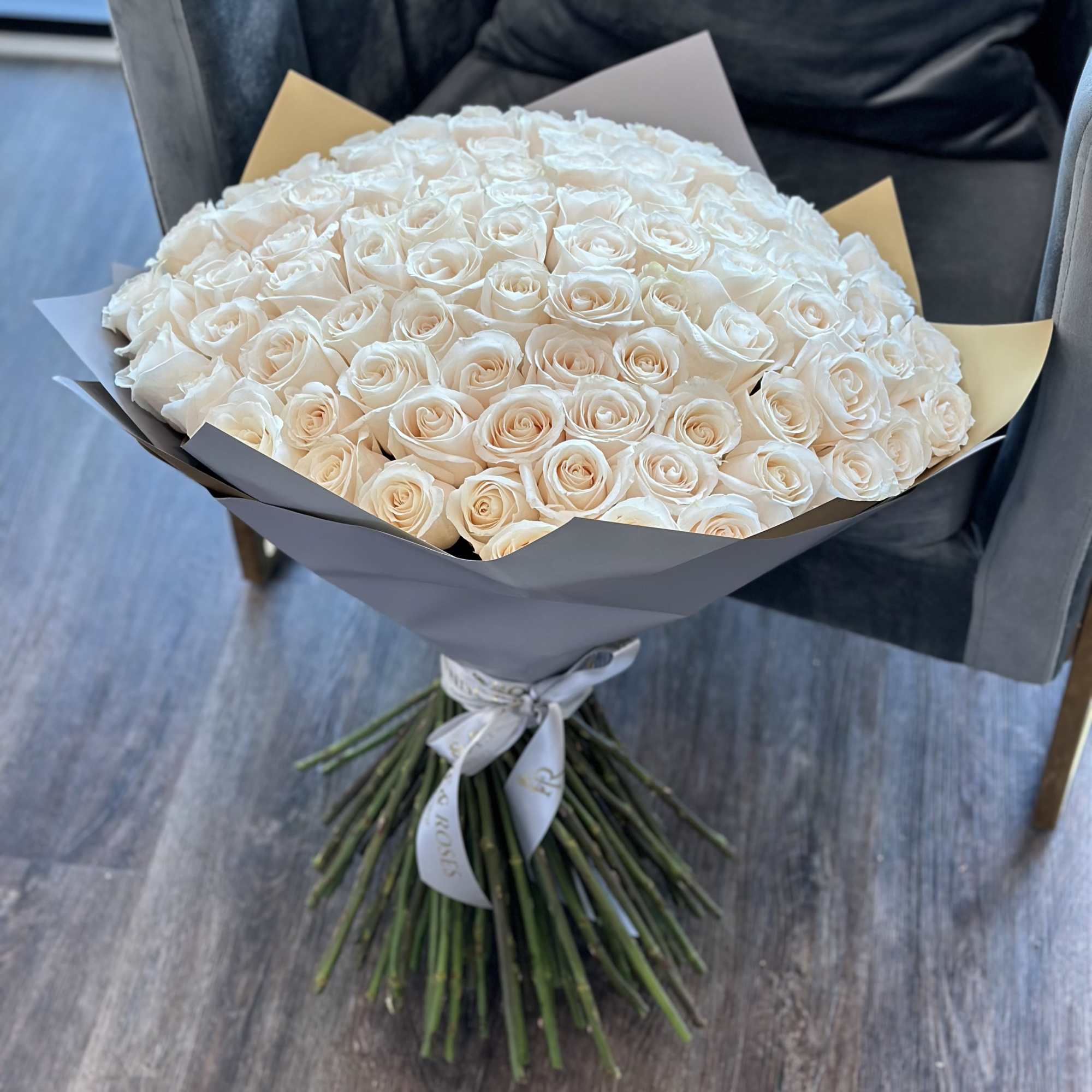 Large bouquet of cream roses wrapped in gray paper with a ribbon