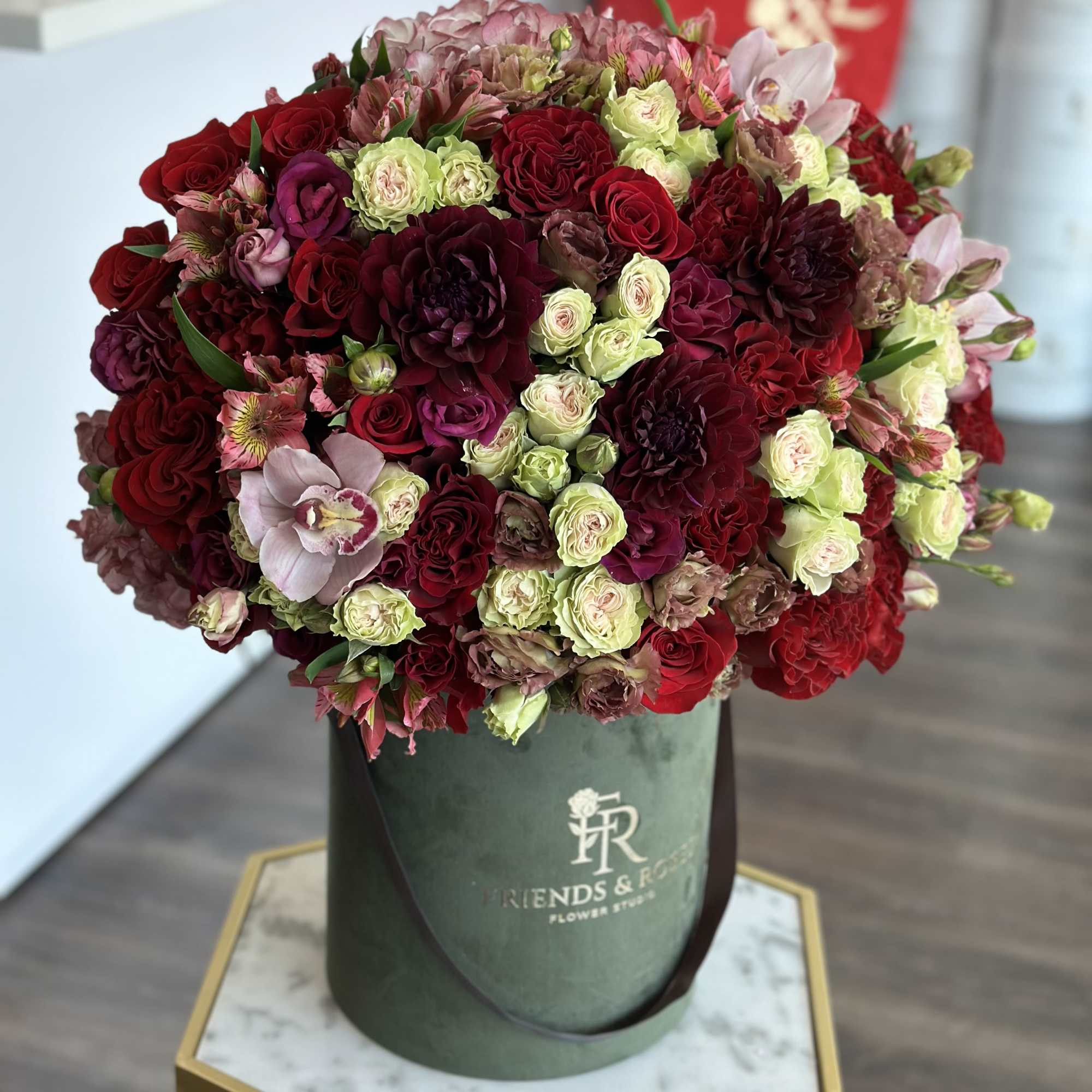 Large bouquet of red, pink, and pale green flowers in a green hatbox