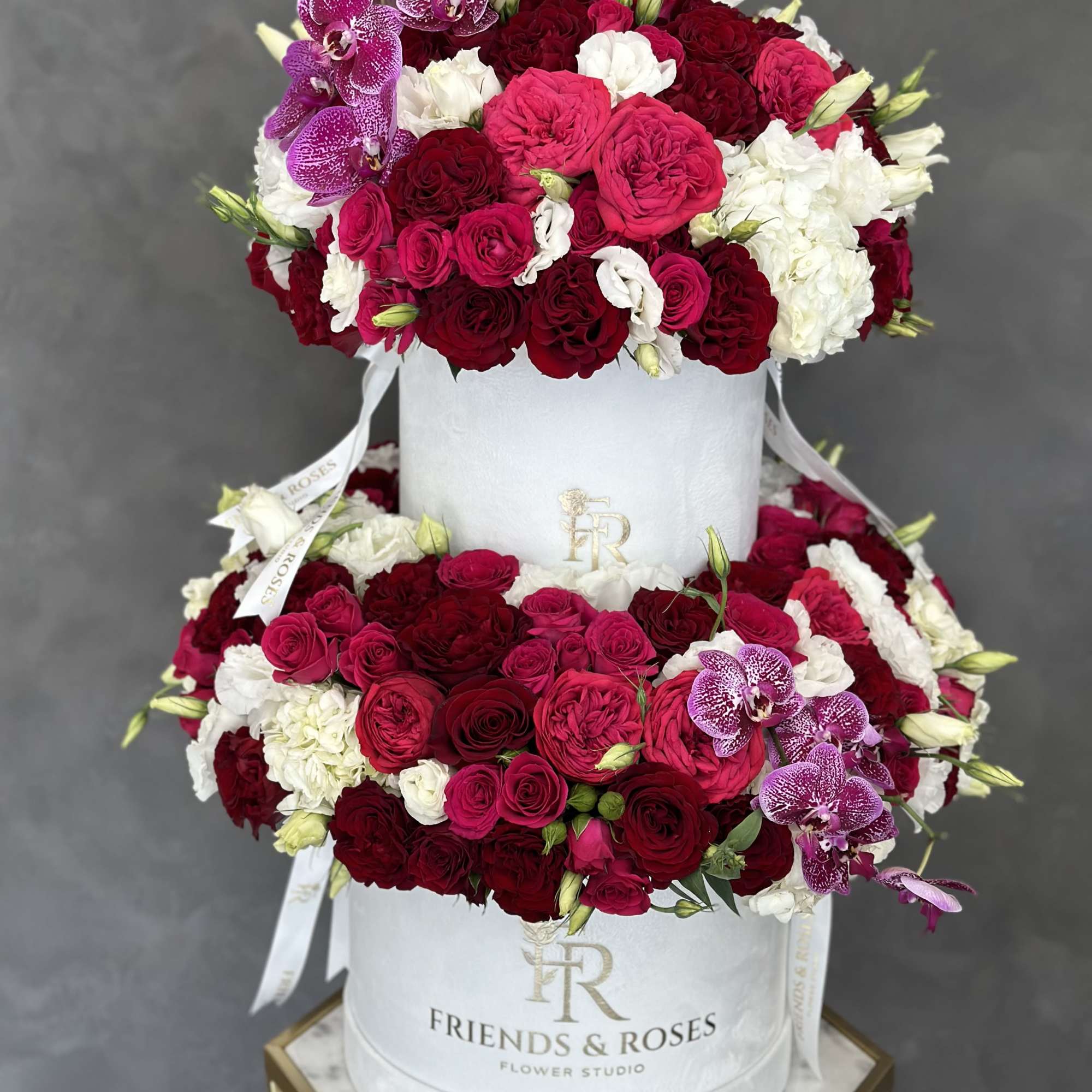 Two-tier rose arrangement in a white hat box with purple orchids