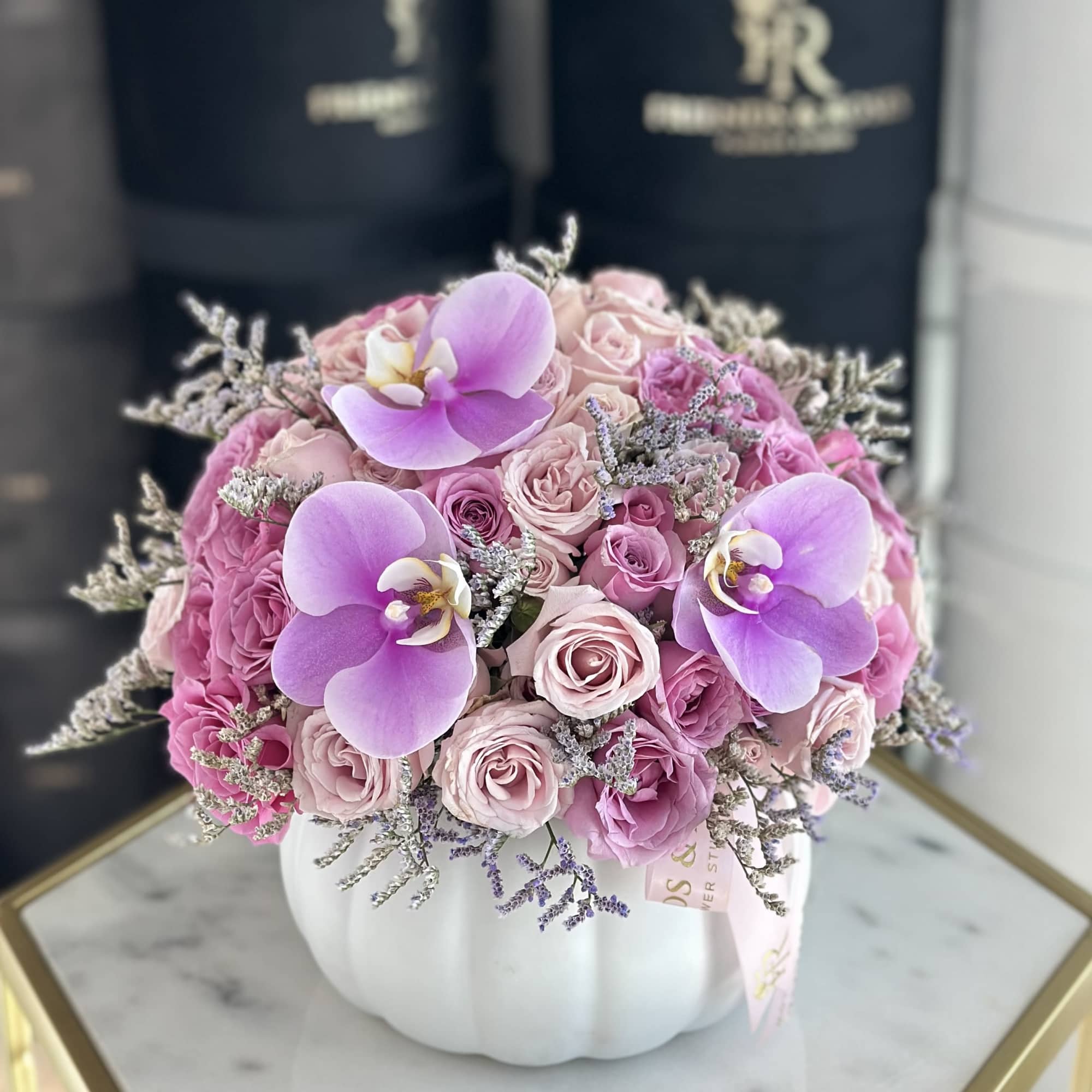 Pink roses and purple orchids arranged in a white pumpkin vase