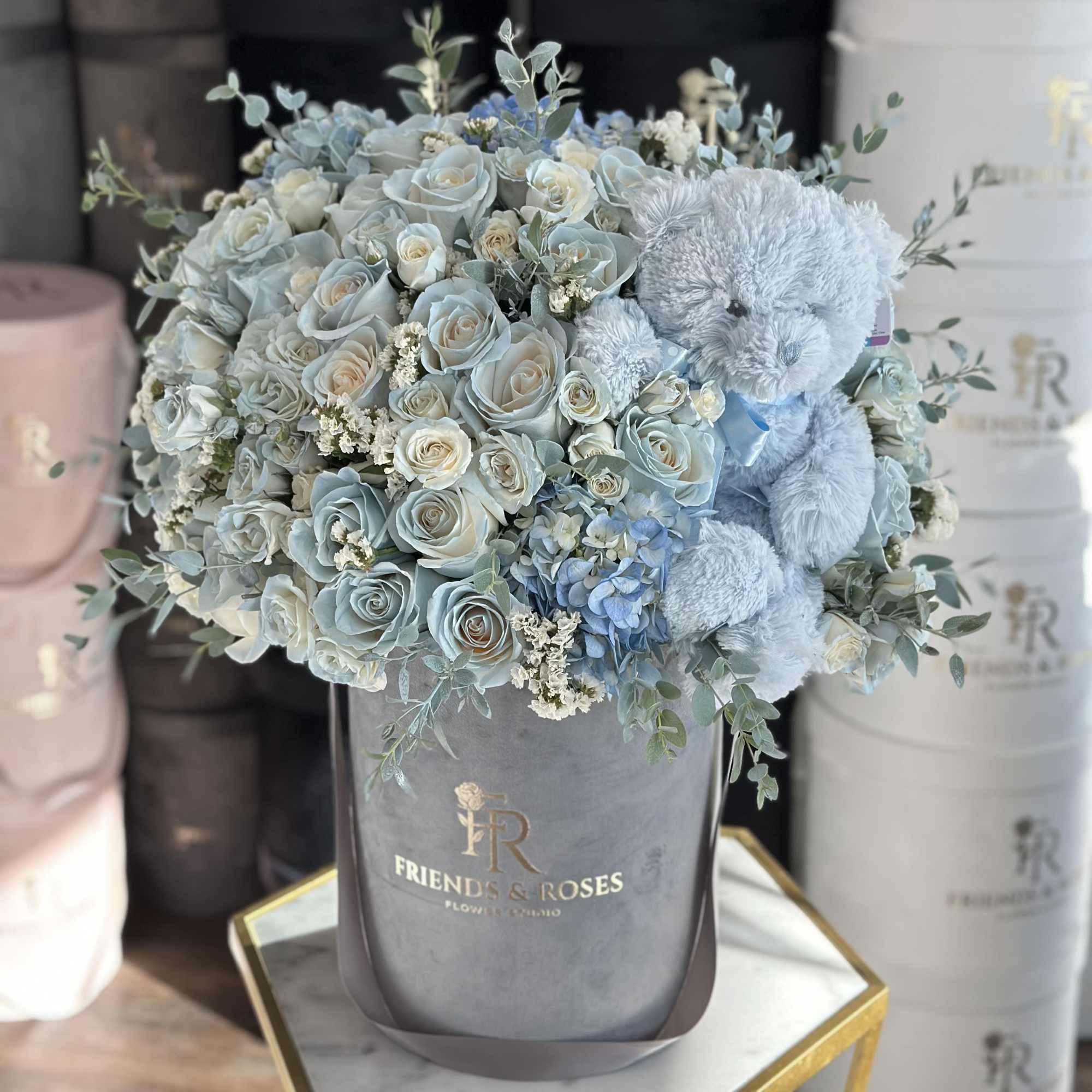 Blue roses and a teddy bear in a gray hatbox