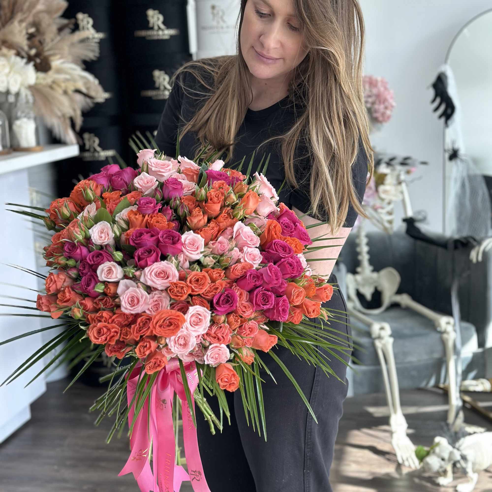 Woman holding a large bouquet of pink and orange roses with a pink ribbon