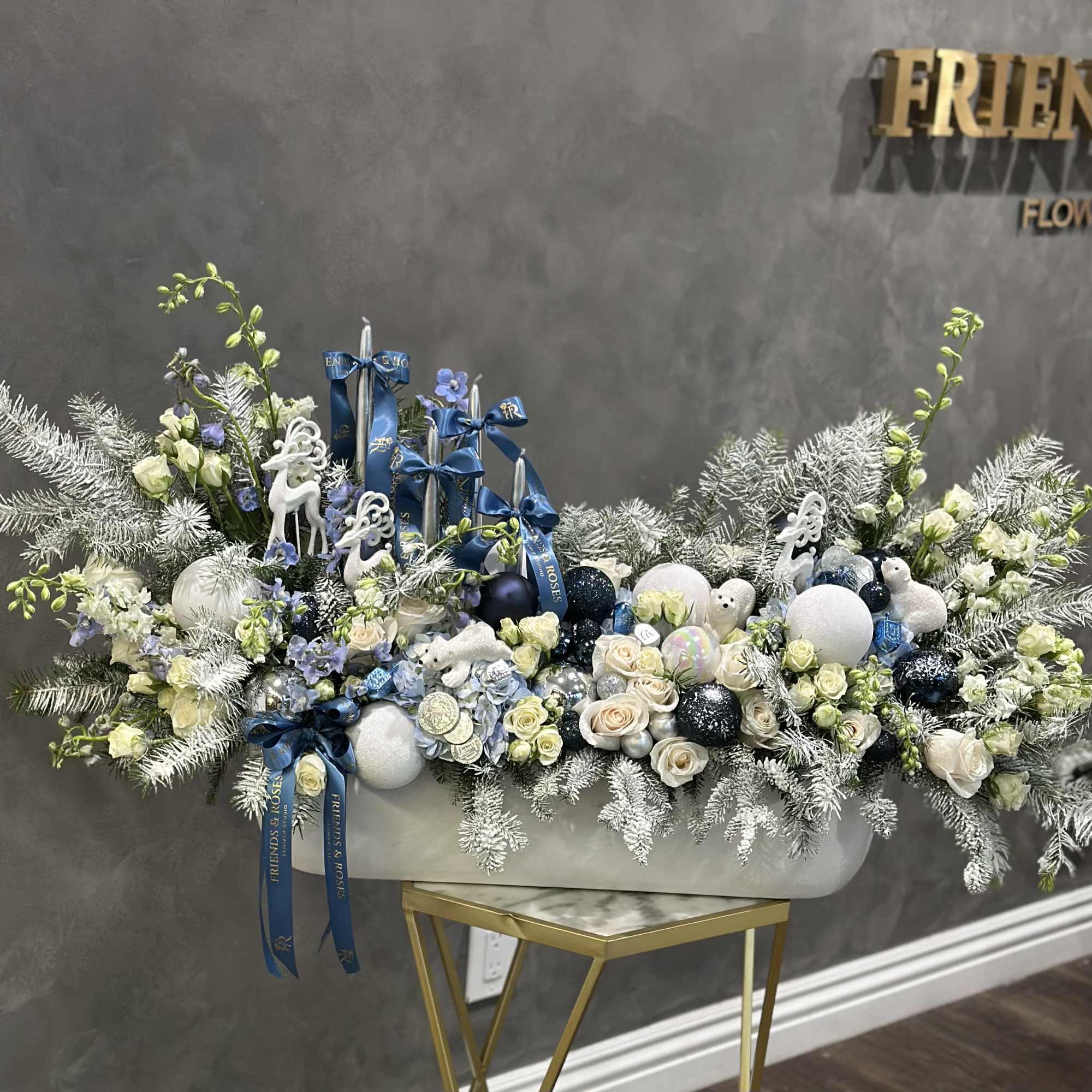 Large white floral arrangement with blue ribbons and ornaments in a white container