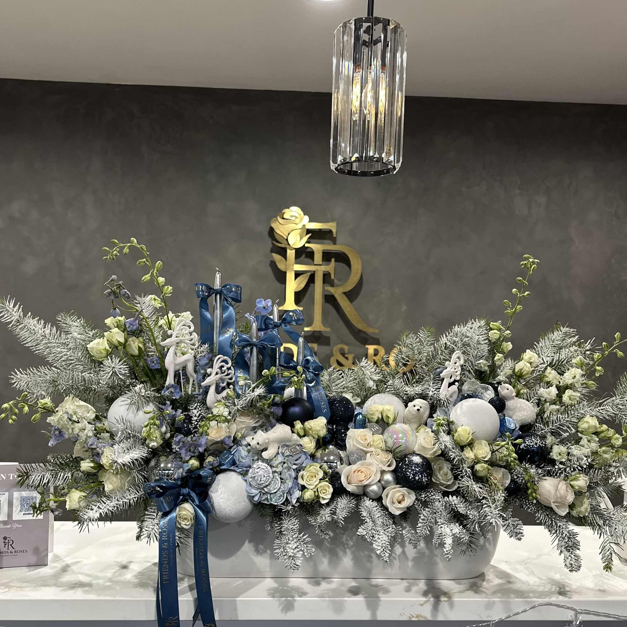Large floral arrangement with white and blue flowers, ornaments, and ribbons in a white container