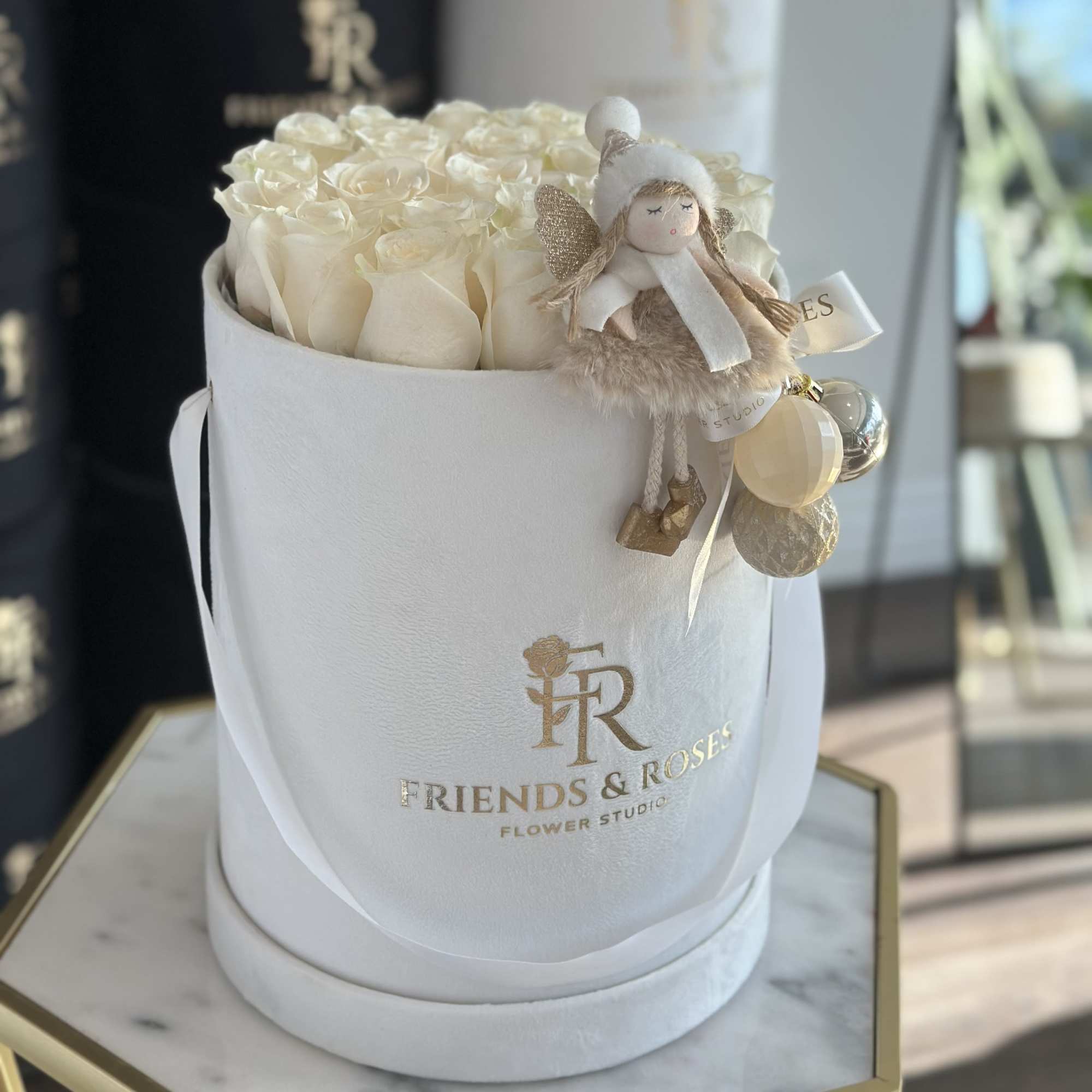 White roses in a round hat box with a small angel ornament