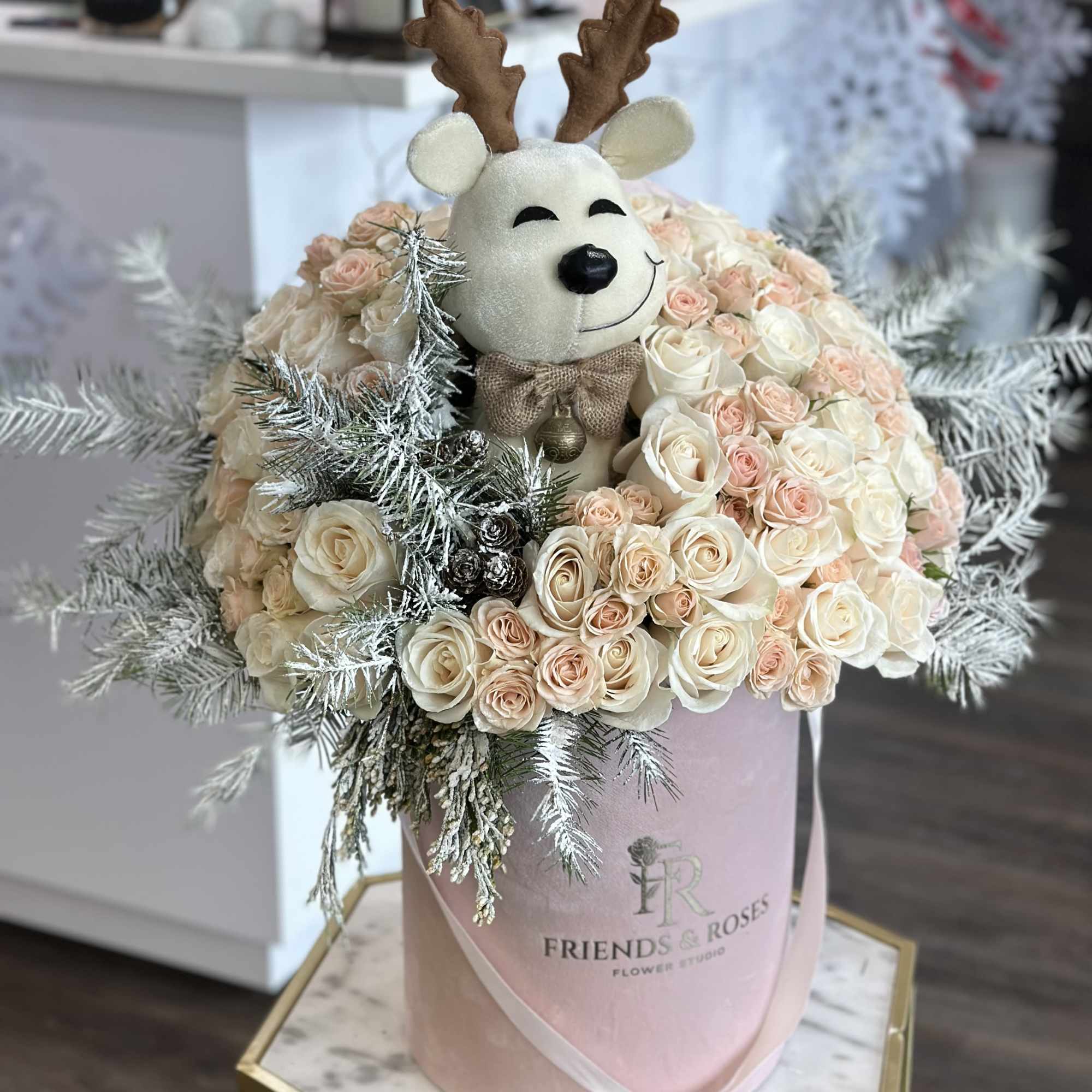 Cream and blush roses in a pink box with a plush reindeer topper