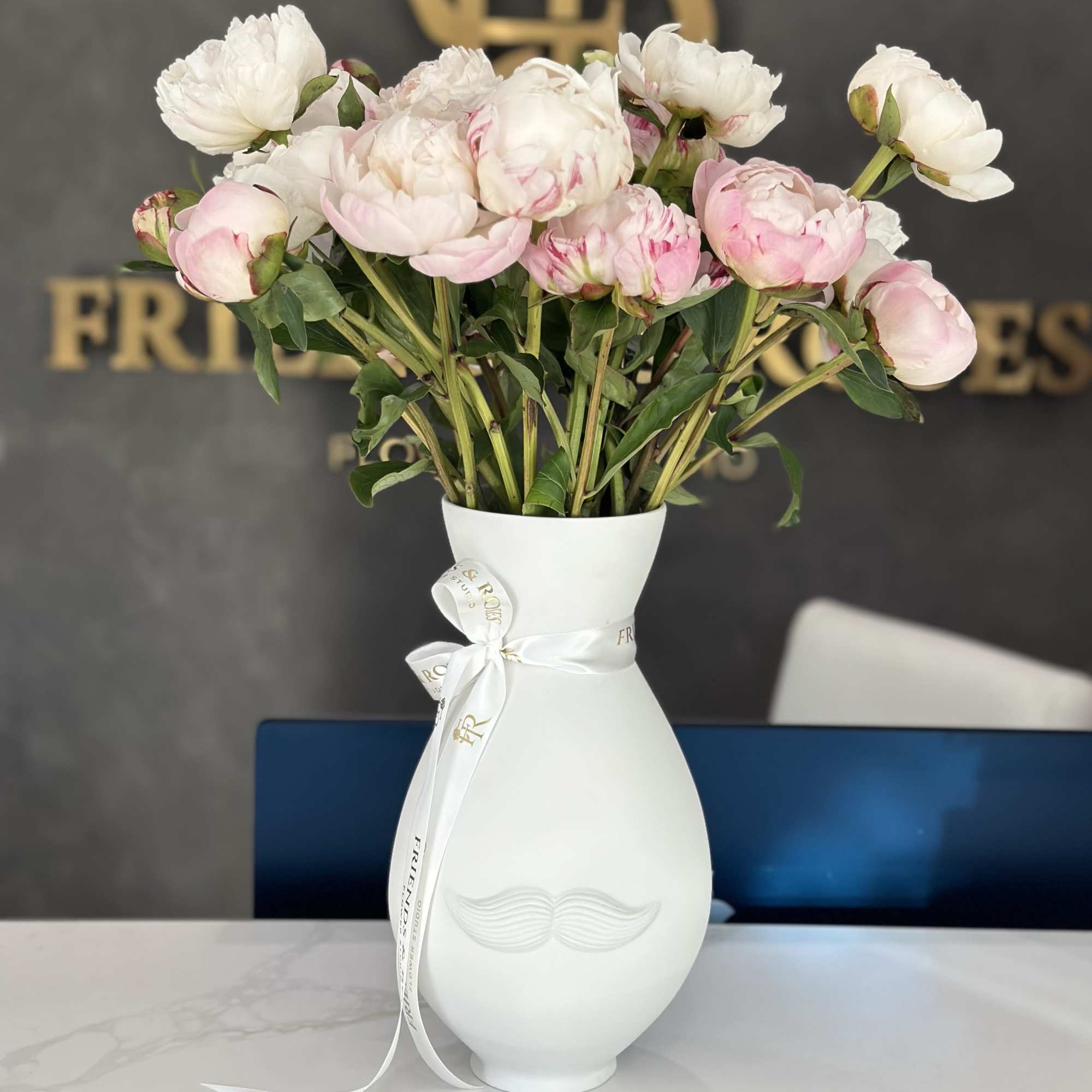 Pink and white peonies arranged in a white vase with a ribbon