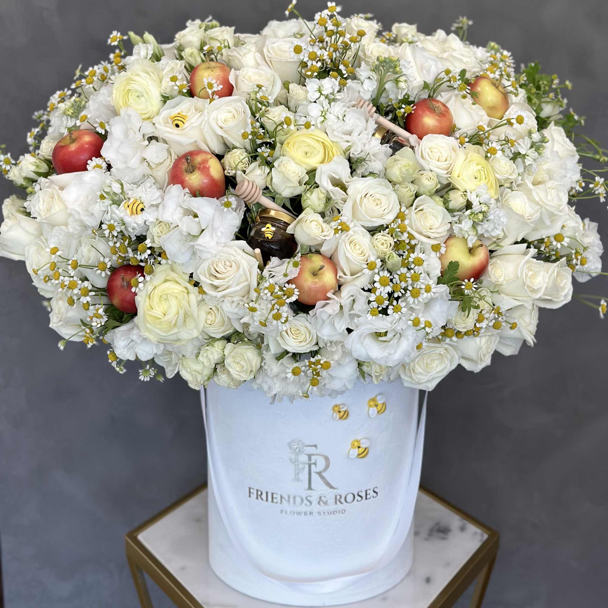 White rose arrangement with apples and small daisies in a white hatbox