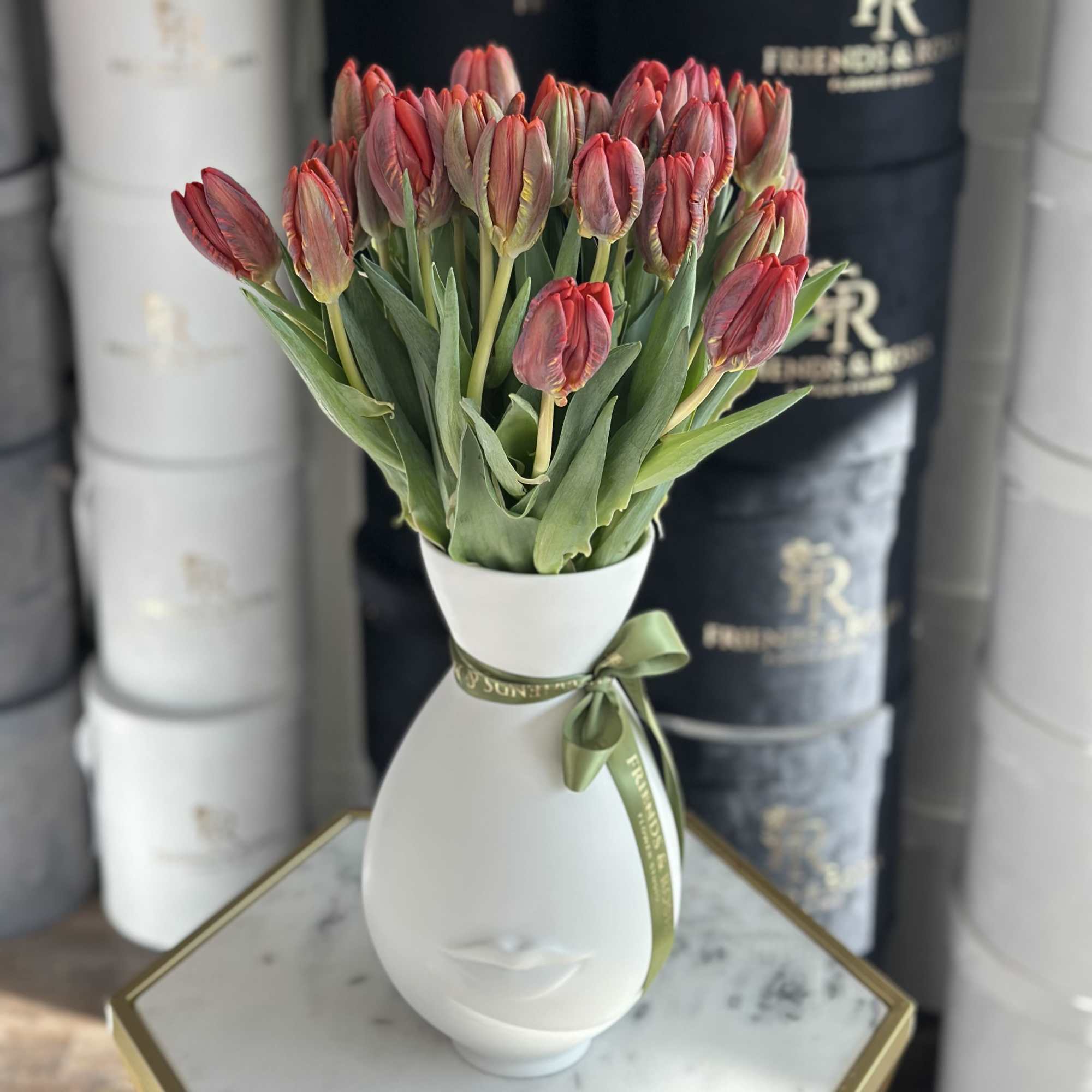 Red tulips arranged in a white face-shaped vase with a green ribbon