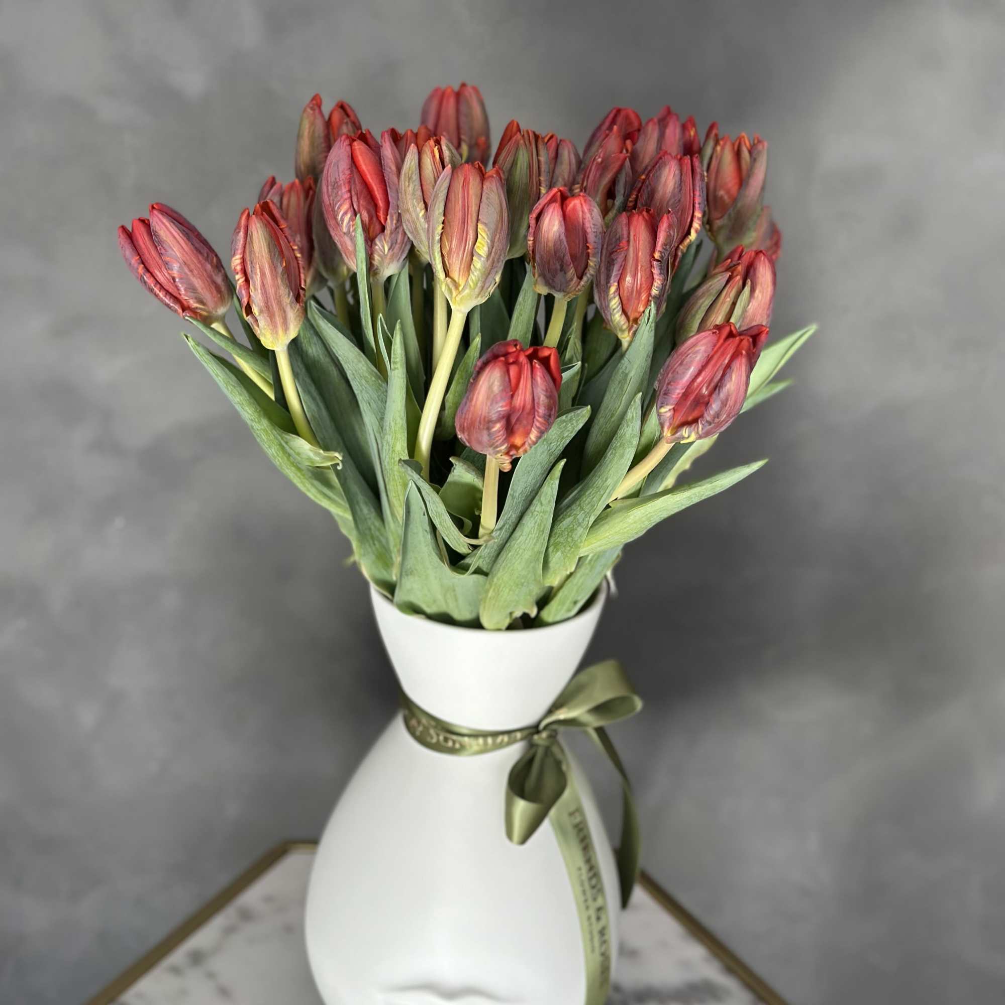 Bouquet of red tulips in a white vase with a ribbon