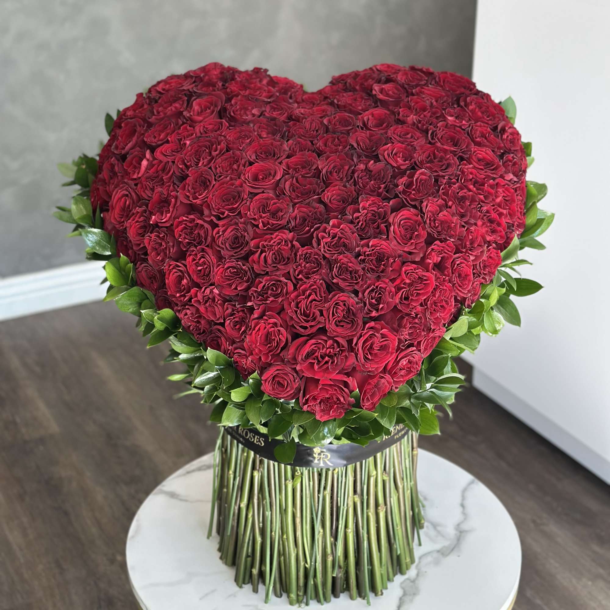 Heart-shaped arrangement of red roses with green foliage on a tall stand