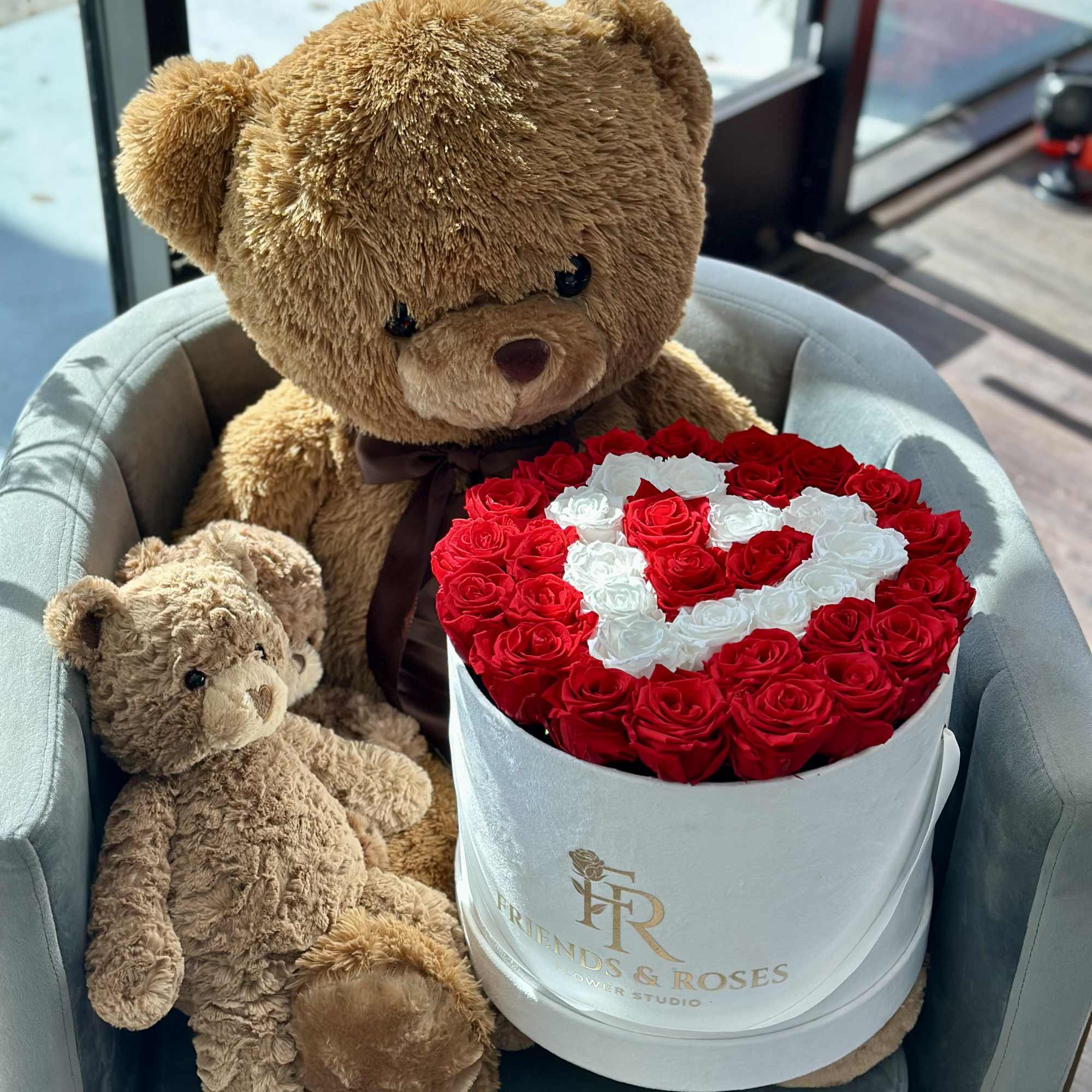 Teddy bears beside a round box of red and white roses