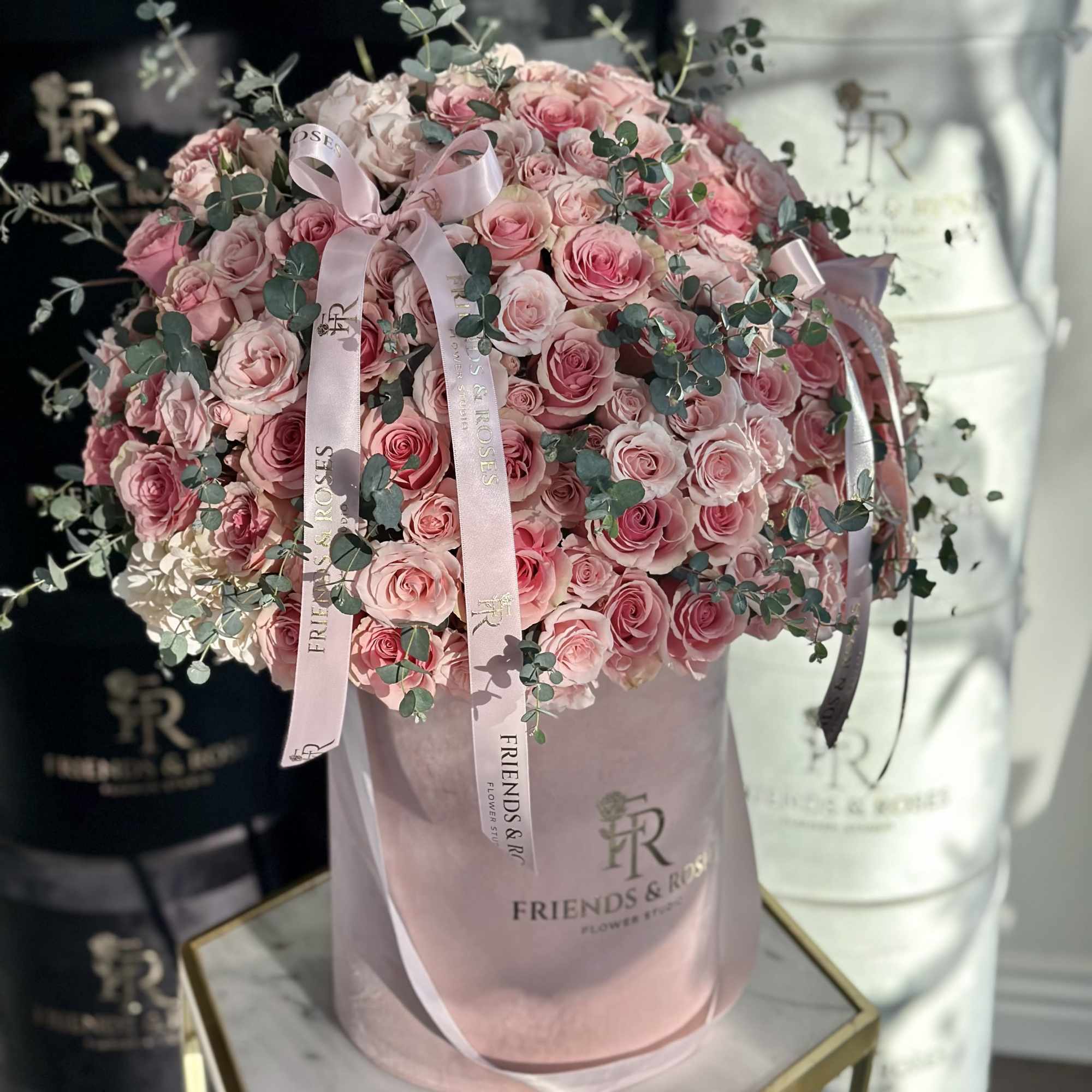 Pink roses arranged in a round hatbox with ribbon and eucalyptus accents