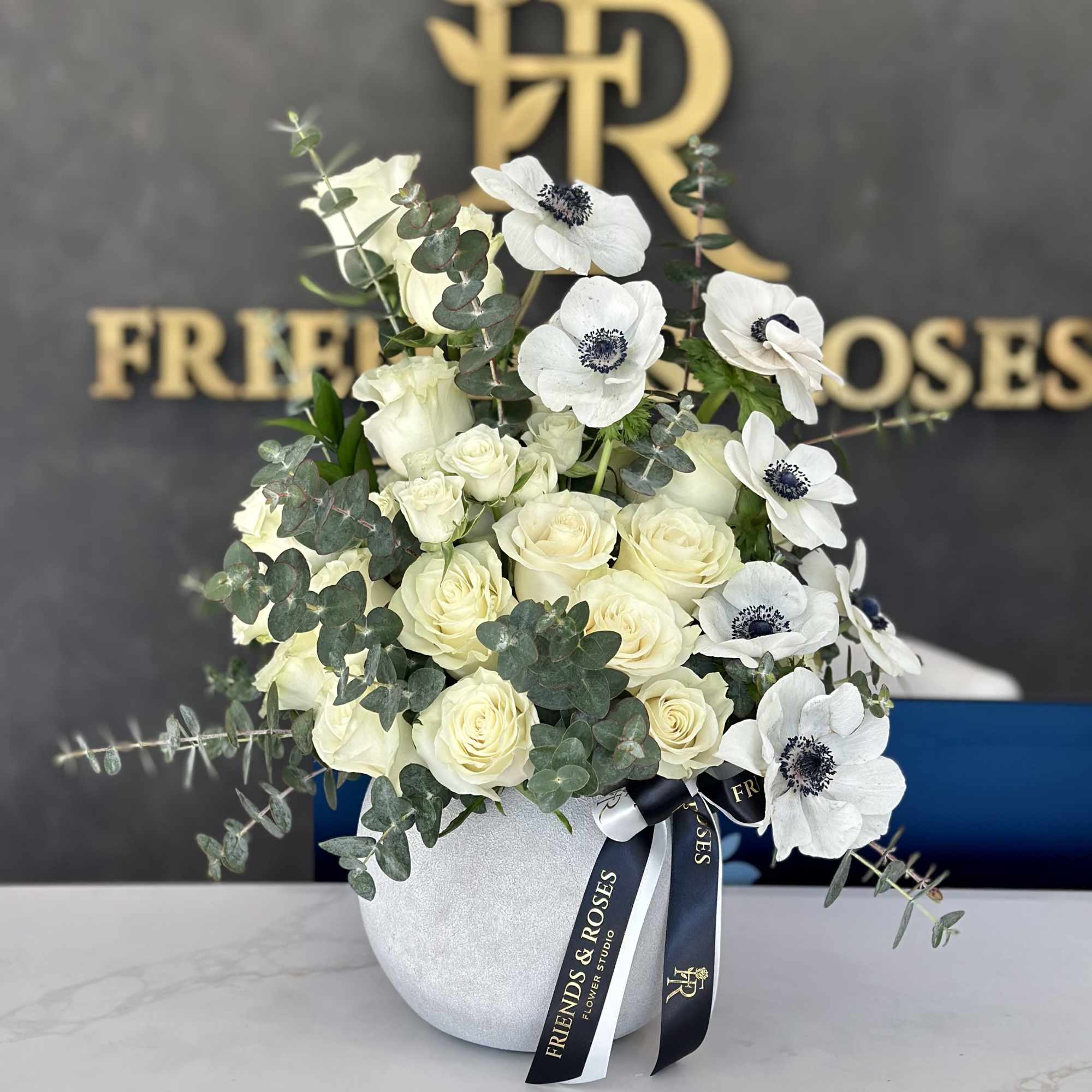 White roses and anemones in a round white vase with eucalyptus