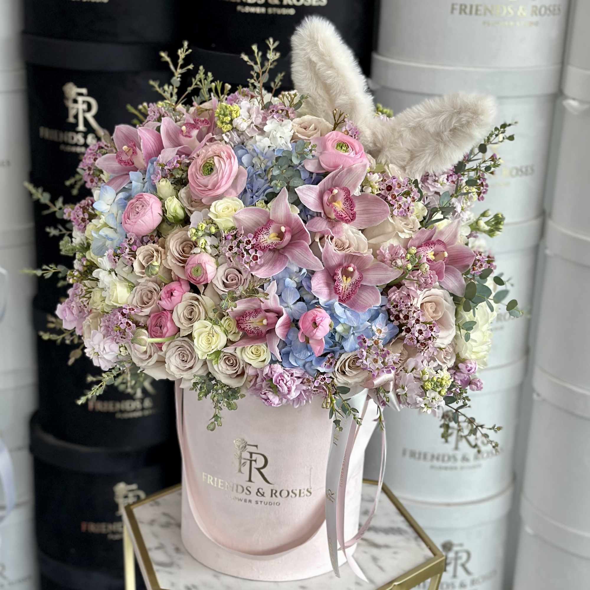 Pink and blue floral arrangement in a pale pink hat box with bunny ears