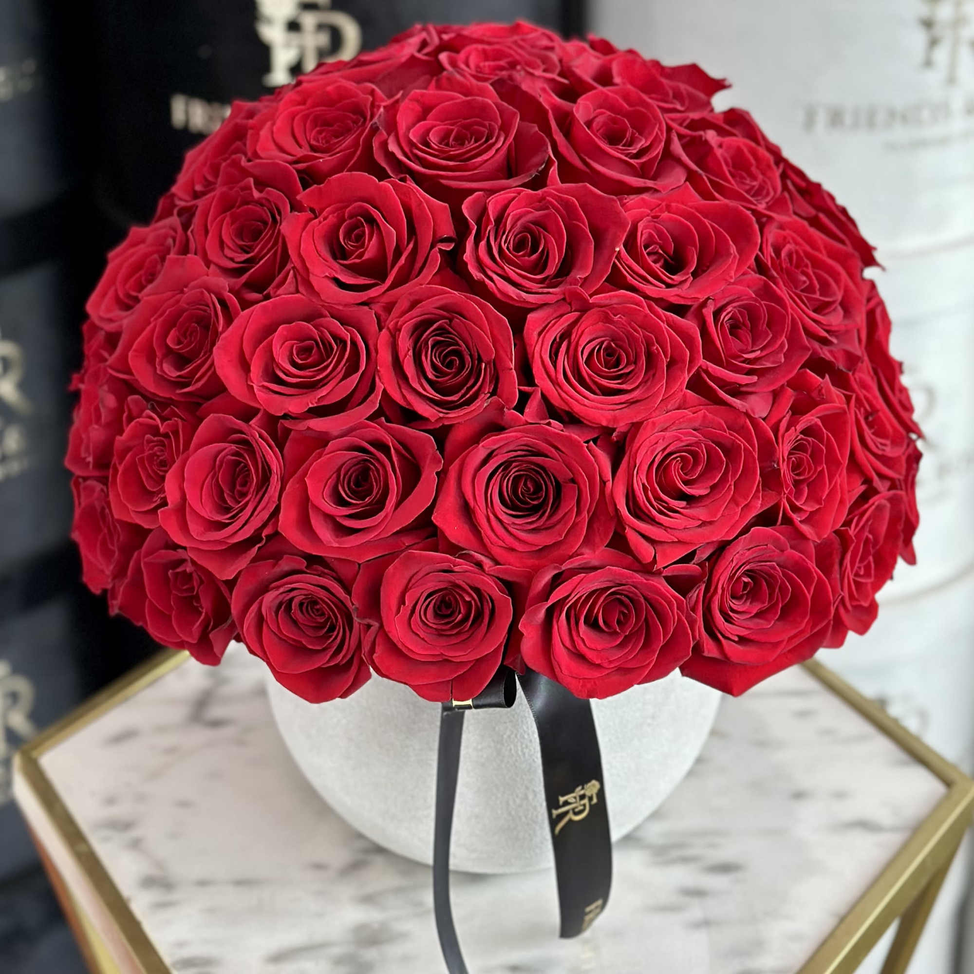 Round bouquet of red roses in a white hat box with a black ribbon