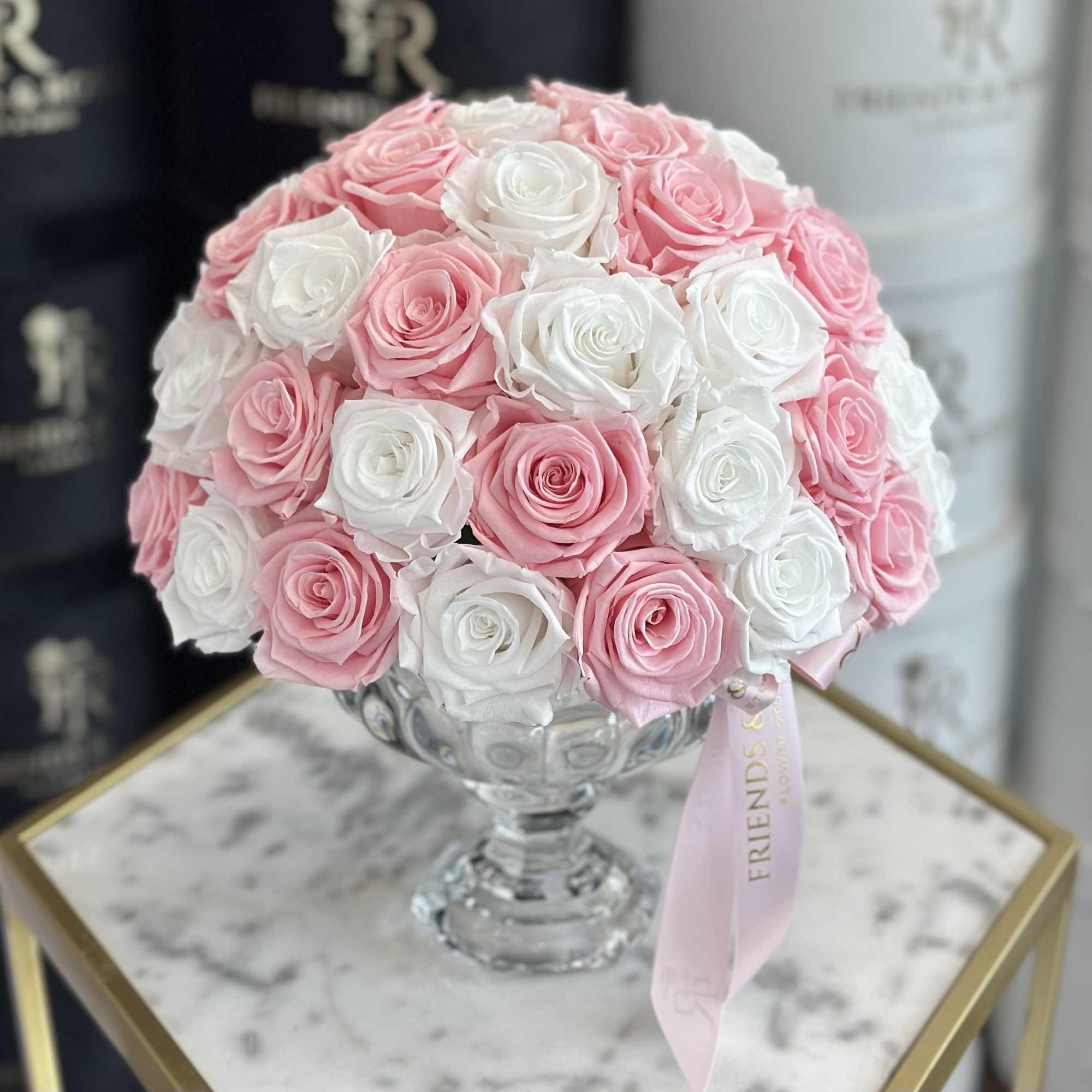 Pink and white rose bouquet in a clear glass vase with a pink ribbon