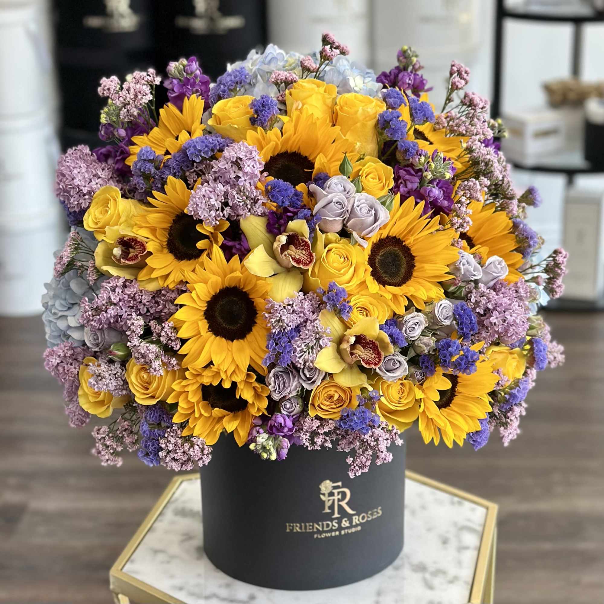 Large bouquet of sunflowers, roses, and purple flowers in a black box
