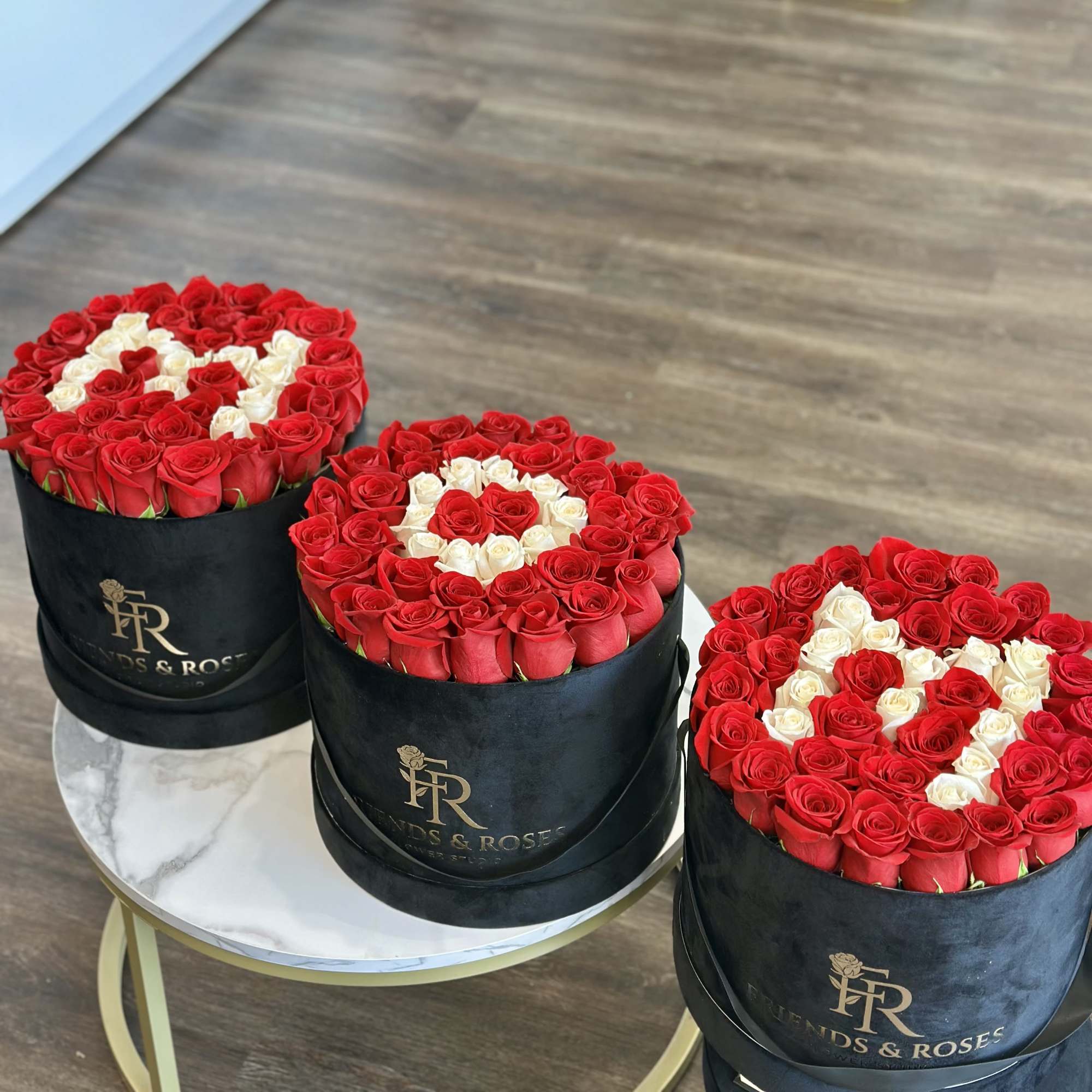 Three round boxes of red and white roses on a table.