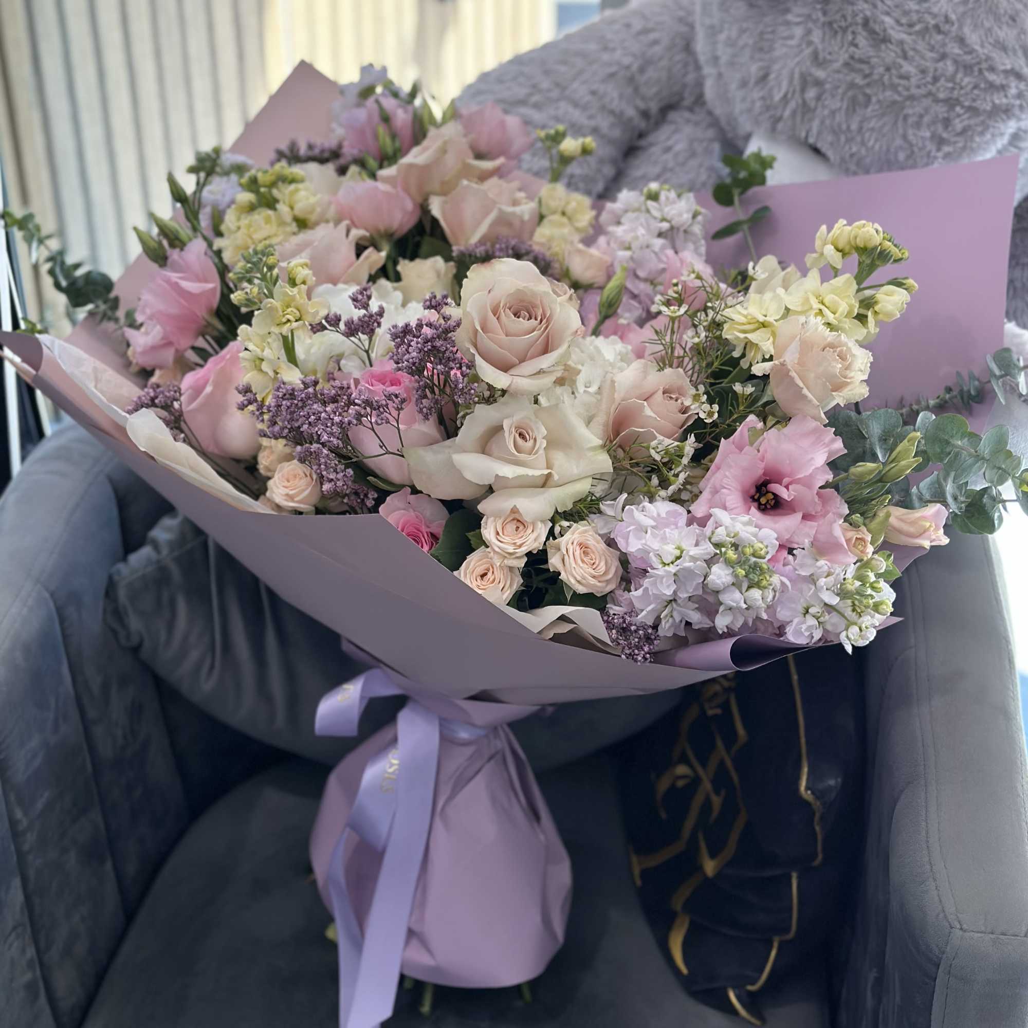 Pastel bouquet of roses, lisianthus, and small filler flowers wrapped in lavender paper
