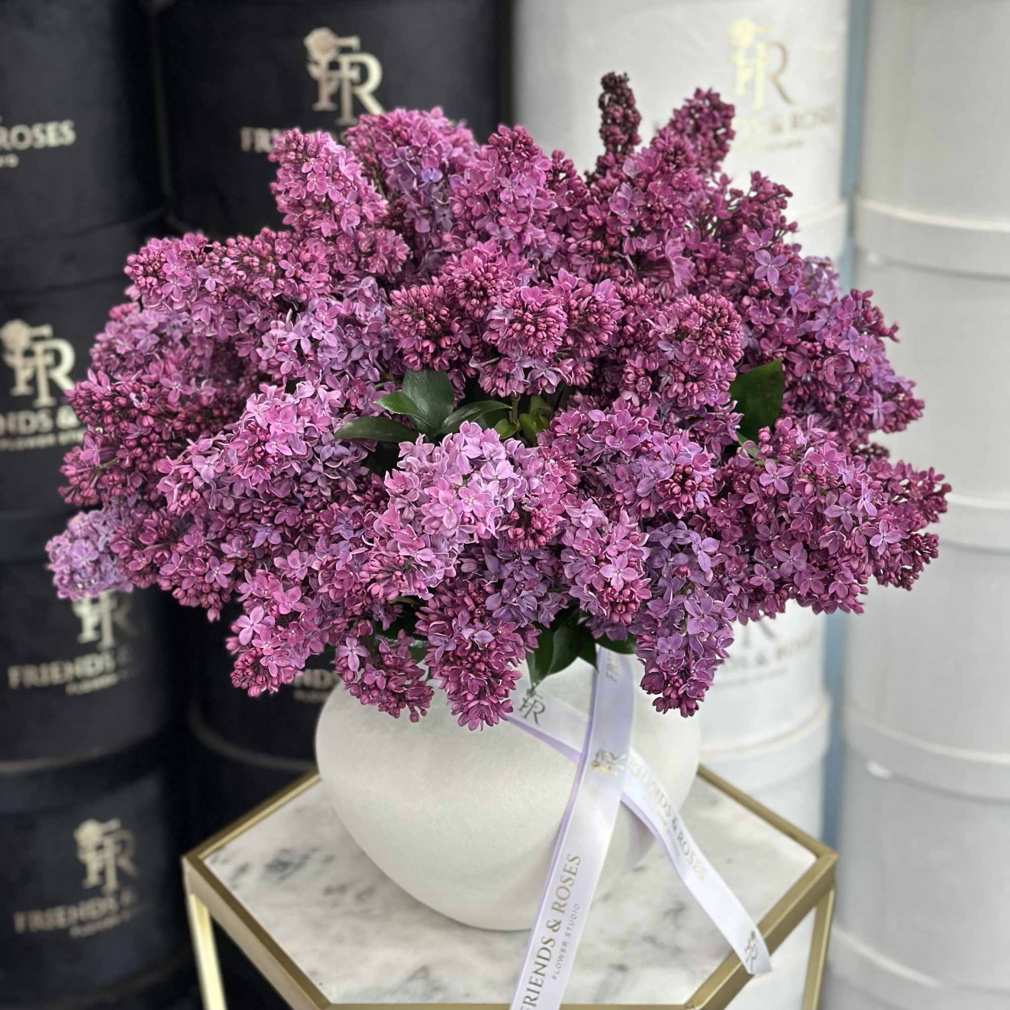 Purple lilac bouquet in a white round vase with ribbon