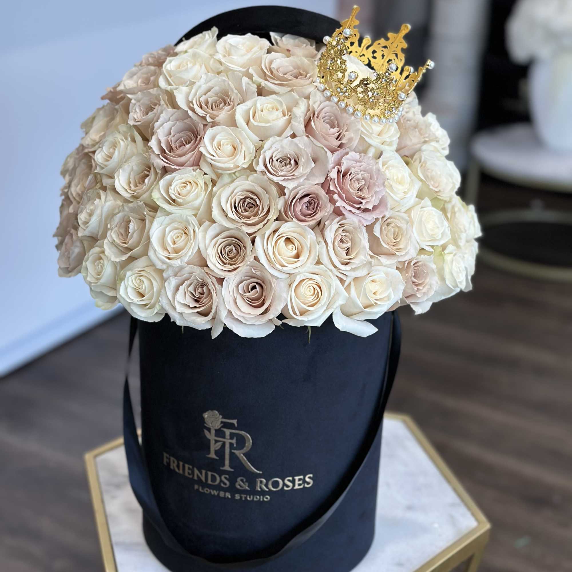 Round bouquet of pale roses in a black hatbox with a gold crown topper