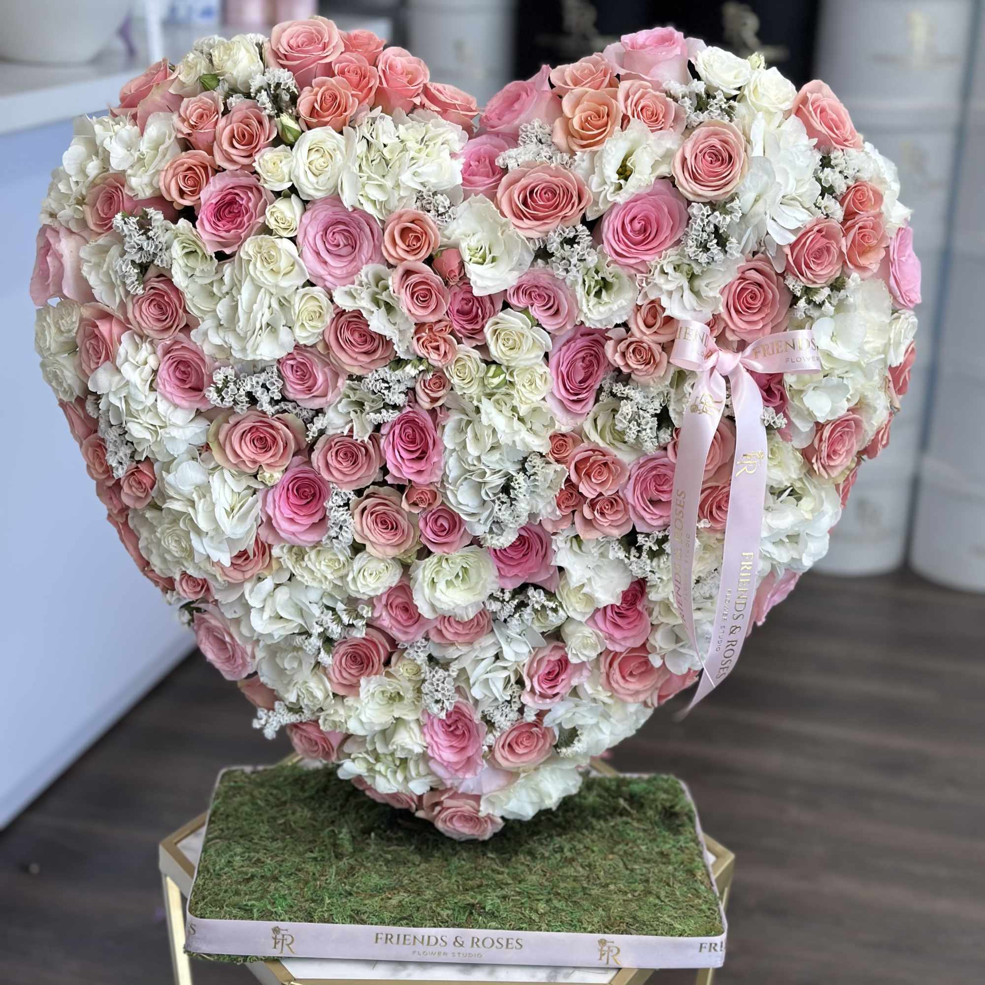 Heart-shaped arrangement of pink and white roses on a moss-covered base