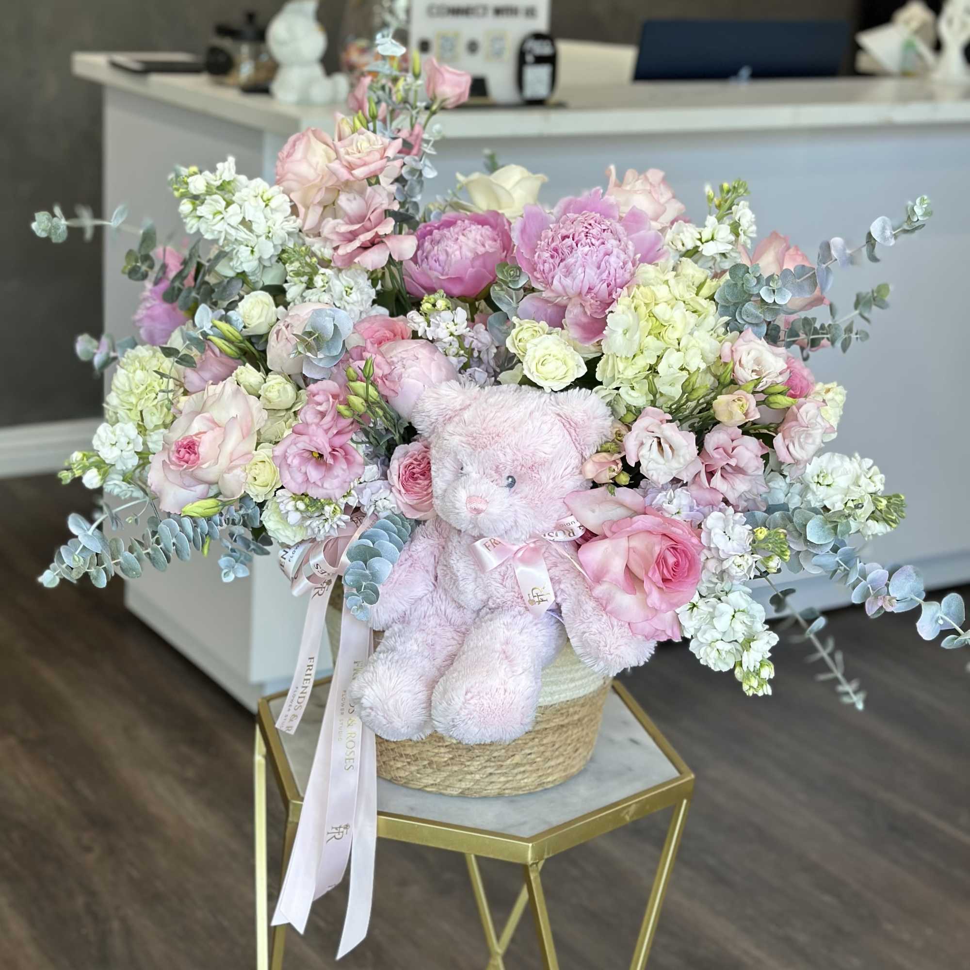 Pink and white flower arrangement with a teddy bear in a woven basket