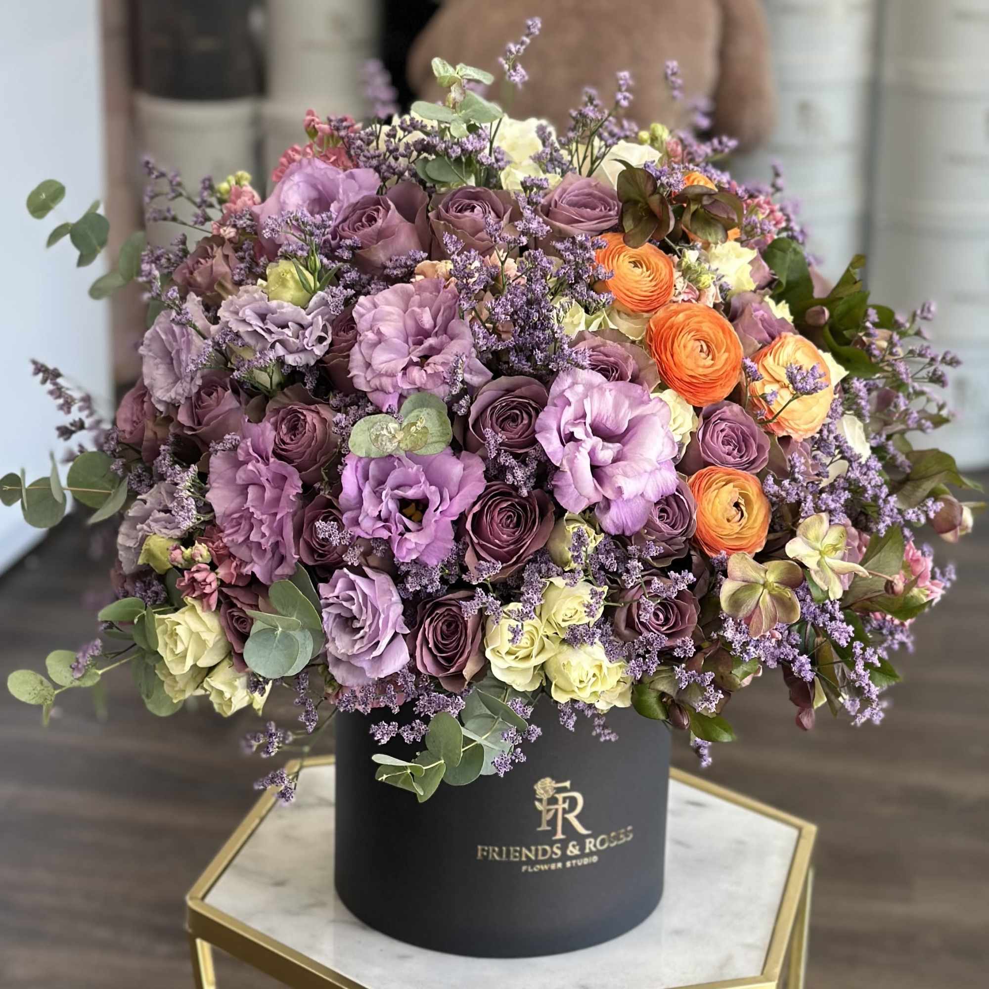 Mixed bouquet of purple, pink, orange, and cream flowers in a black hat box