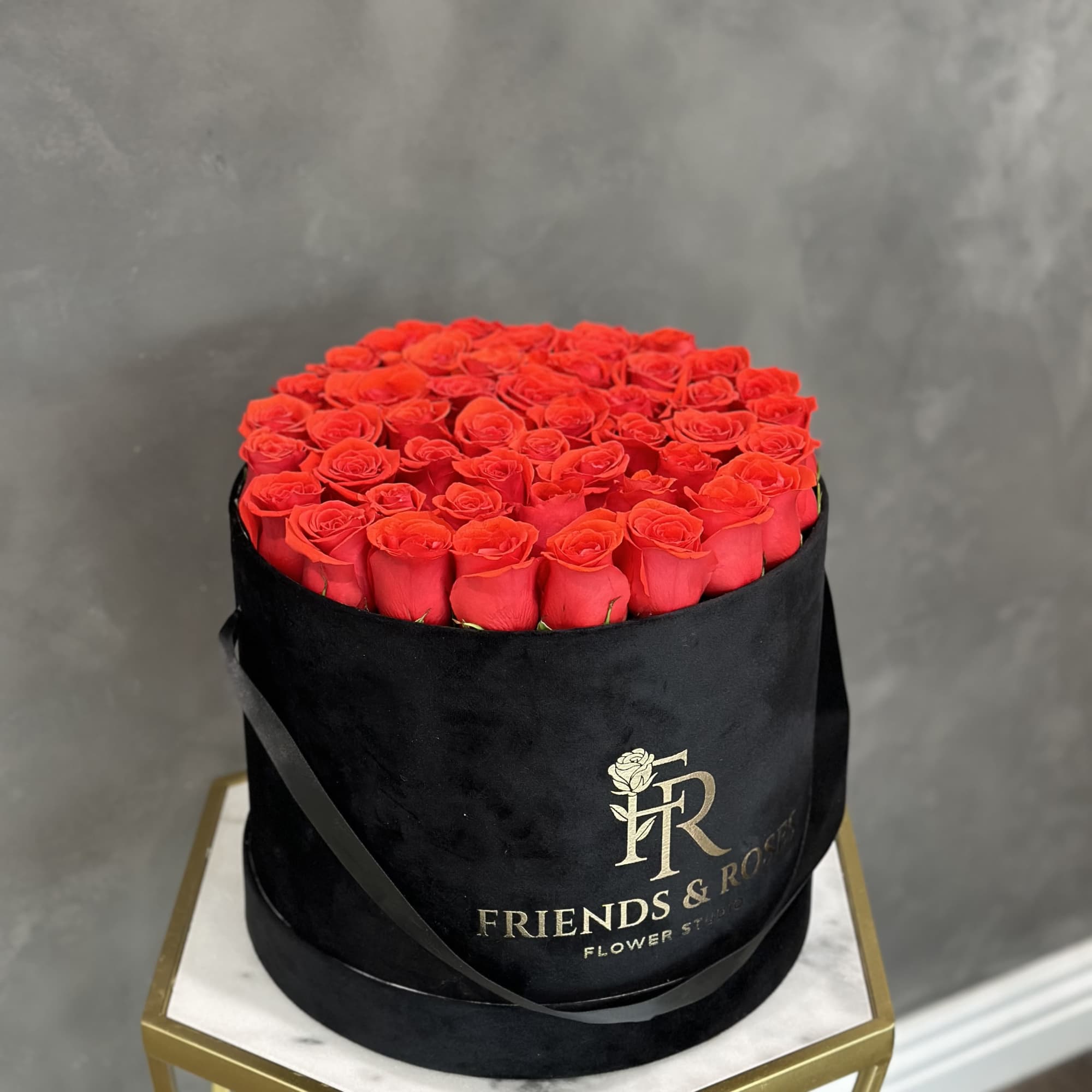 Round box filled with red roses and wrapped in black ribbon