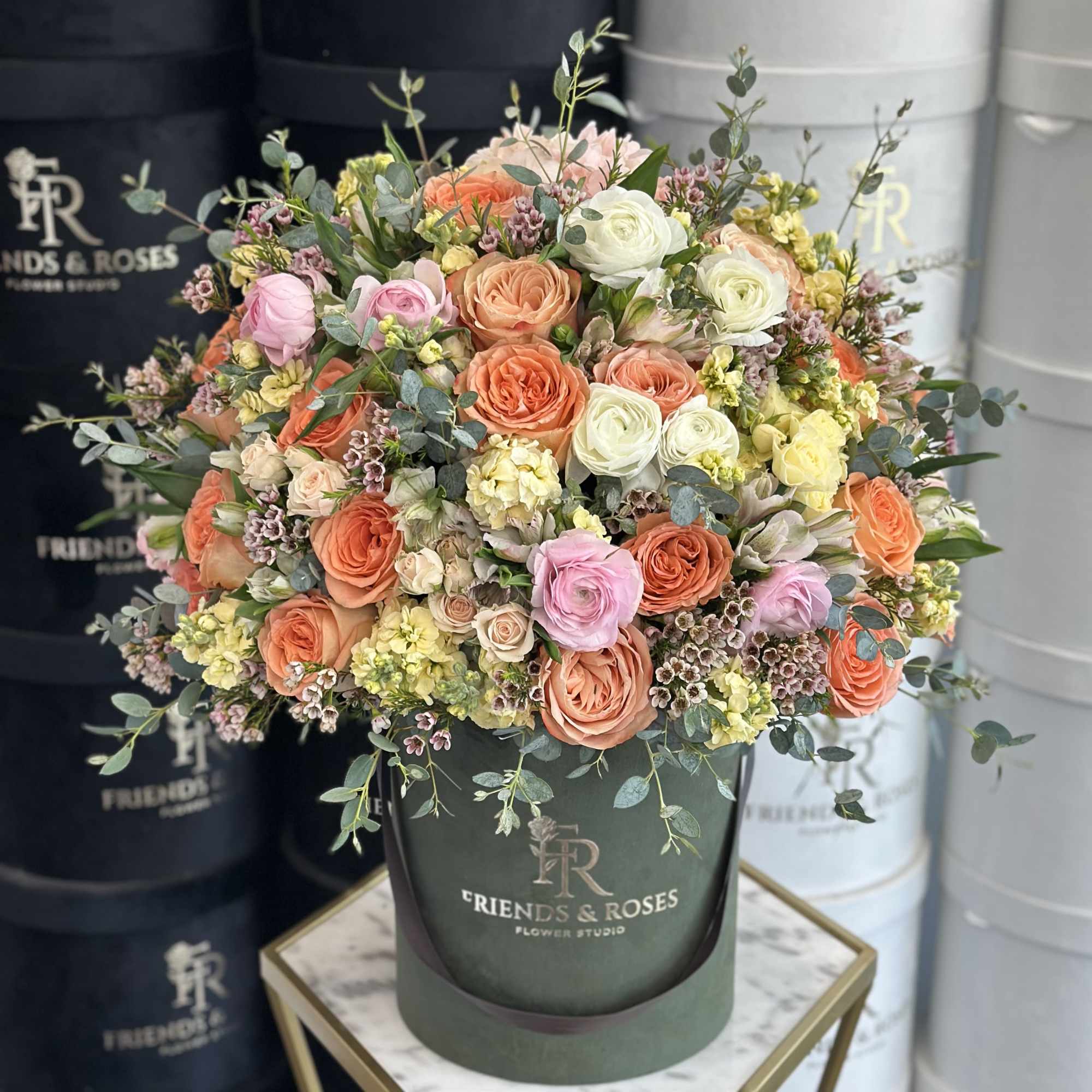 Mixed bouquet of roses and small blooms in a dark green hatbox