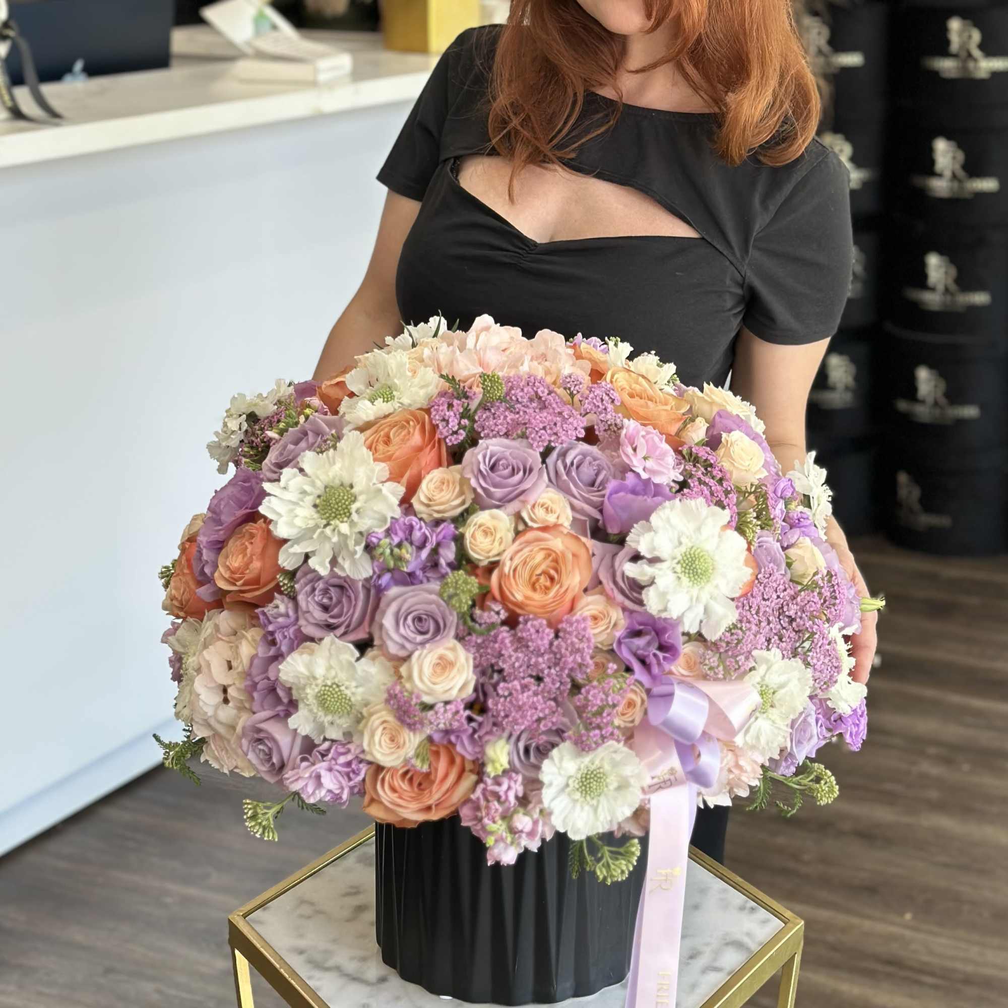 Large pastel bouquet of roses, daisies, and lilac flowers in a black vase