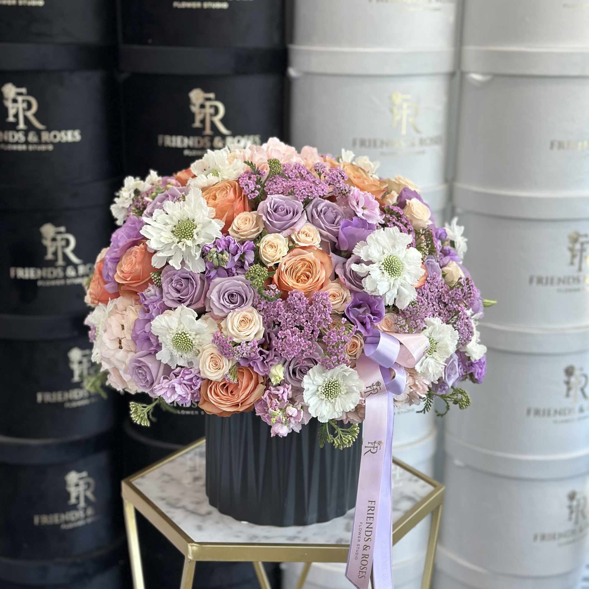 Round bouquet of pastel roses and white daisies in a black hat box