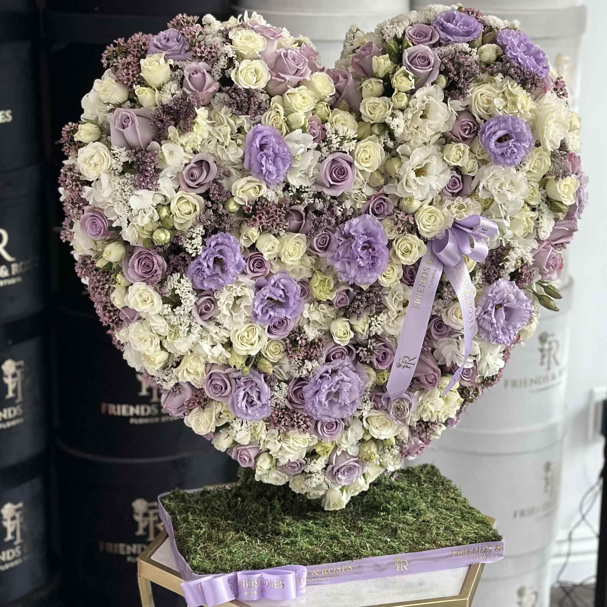 Heart-shaped bouquet of lavender and white roses with ribbon on a moss-covered base